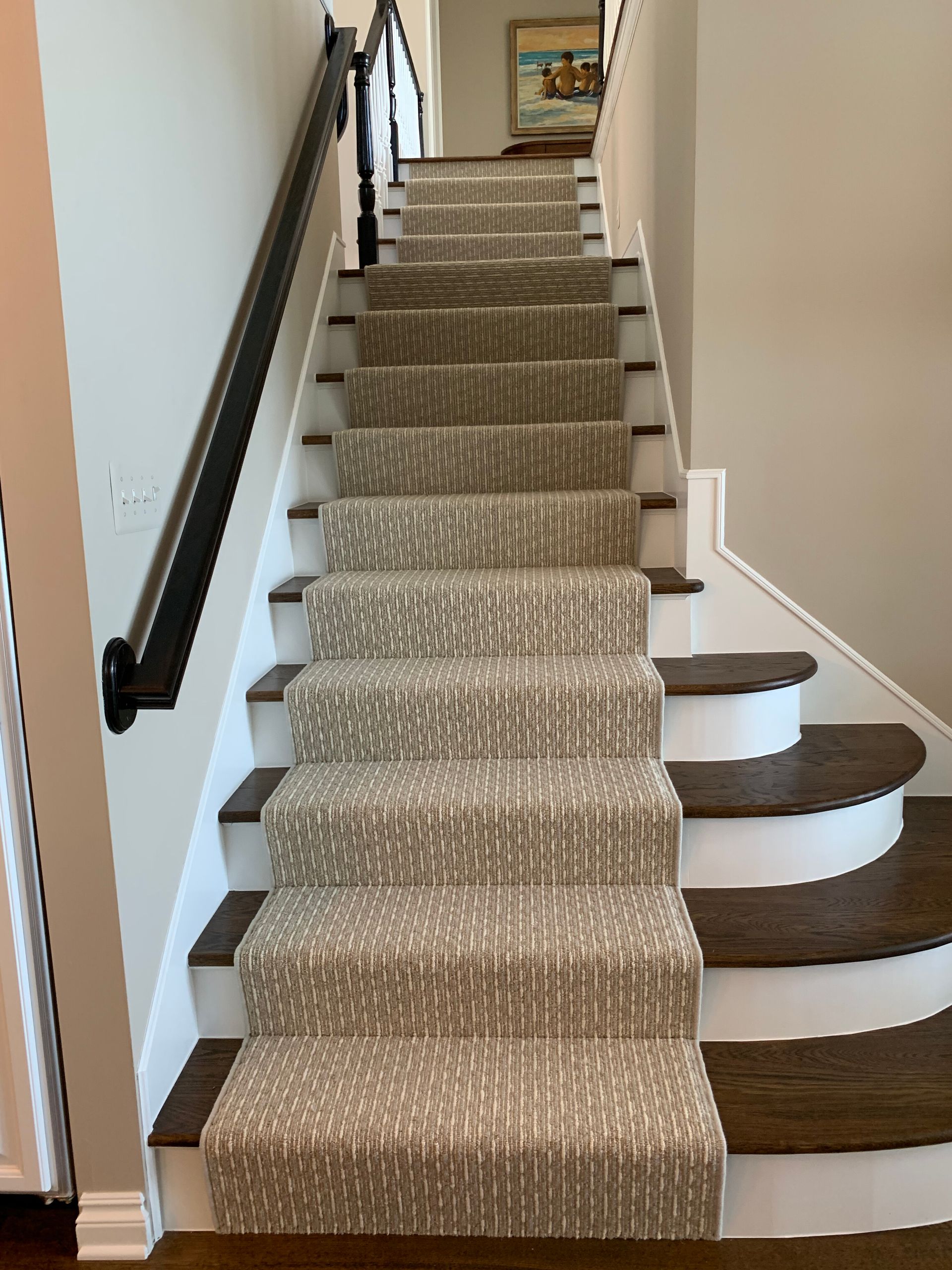 Staircase with carpet runner, dark wood treads, white risers, and a black handrail against a beige wall.