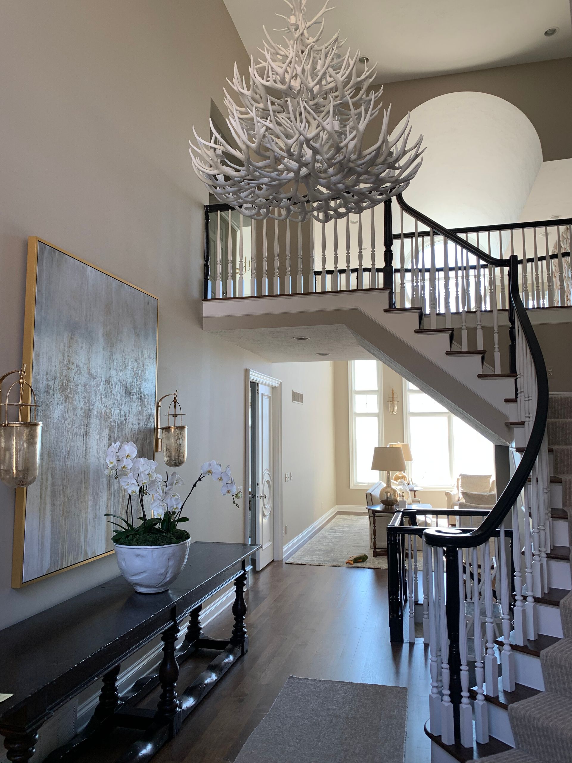 Elegant entry hall with winding staircase, chandelier, artwork, and a console table with orchids.