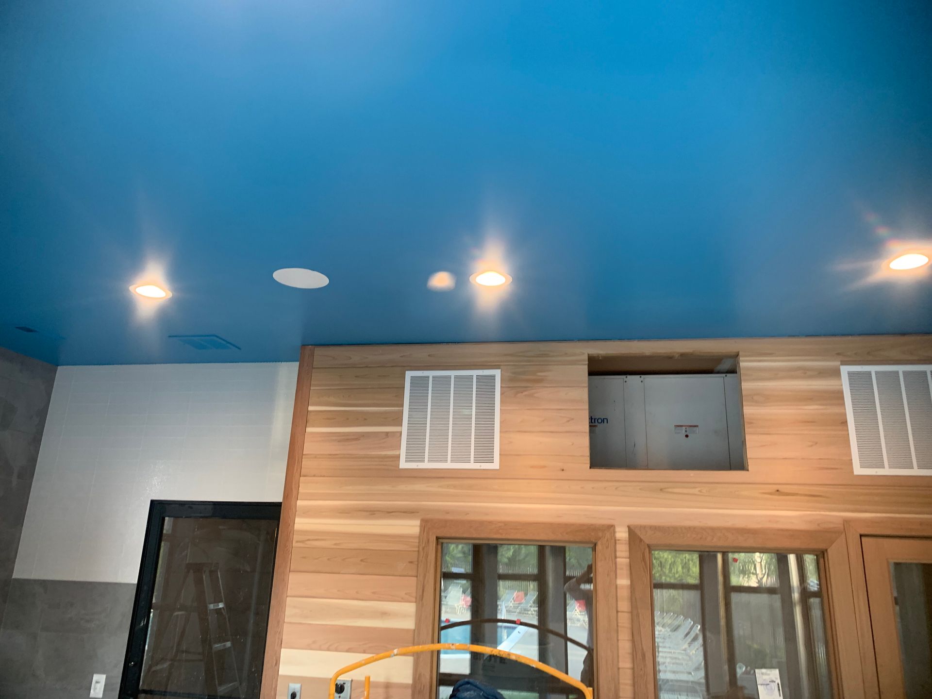 Blue ceiling with recessed lights, wooden wall with vents and openings, windows below.