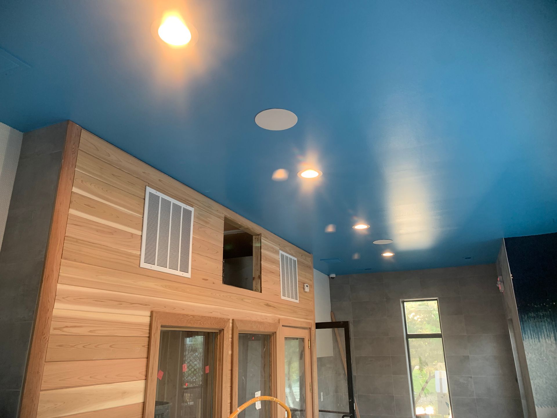 Blue ceiling with recessed lights above a wooden wall with windows.