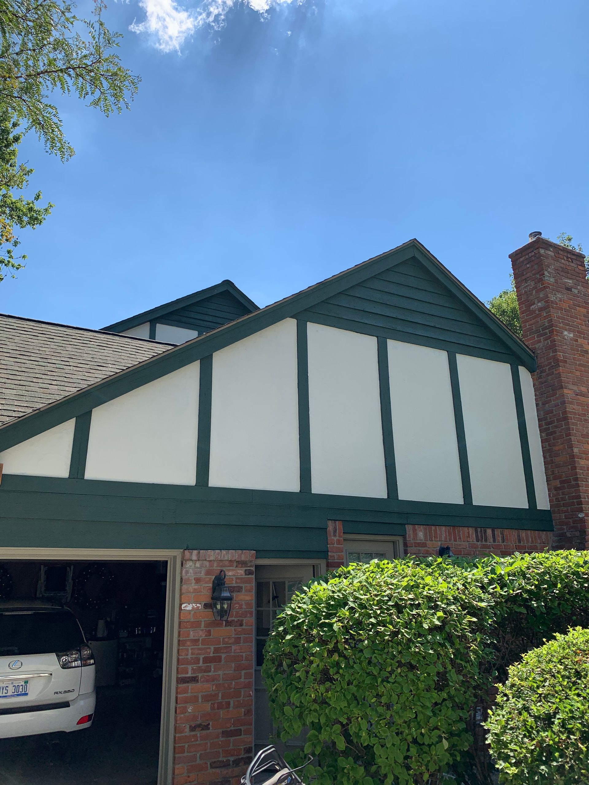 Green and white house exterior with a garage and red brick chimney under a blue sky.