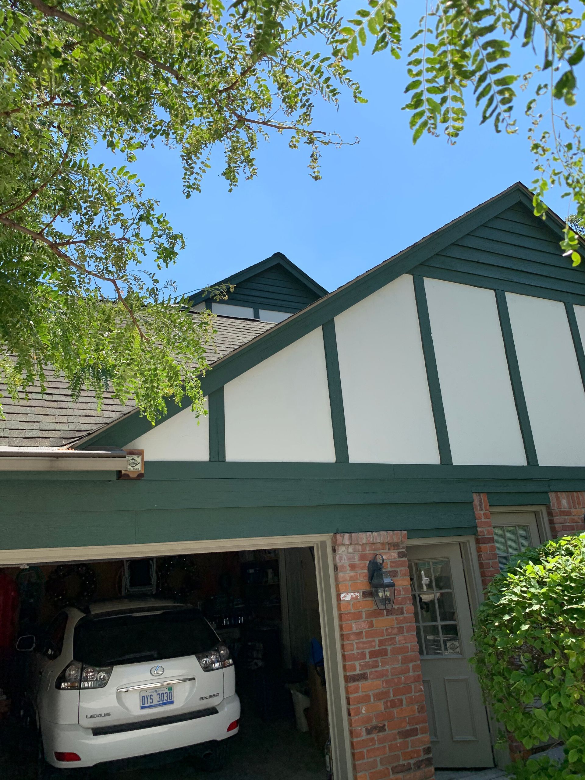 Green and white house with a garage, blue sky above, and a car parked inside.