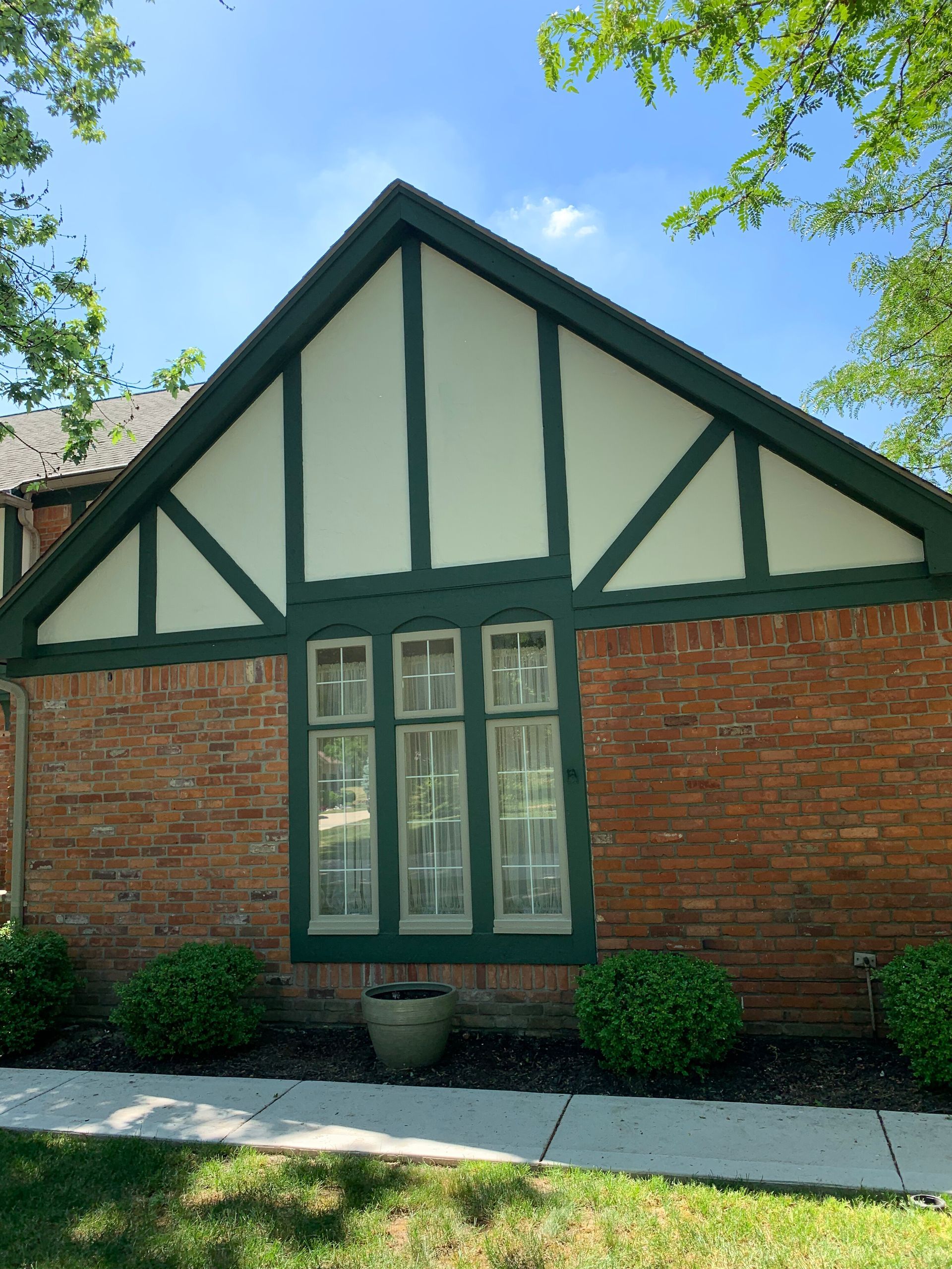 Brick building with green and white trim, triangular peak, and multi-pane window.