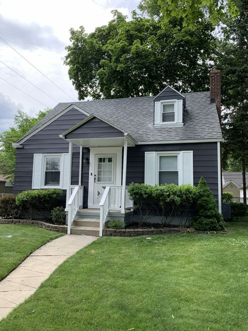 Small, gray house with white trim, porch, and a winding sidewalk on a grassy lawn.