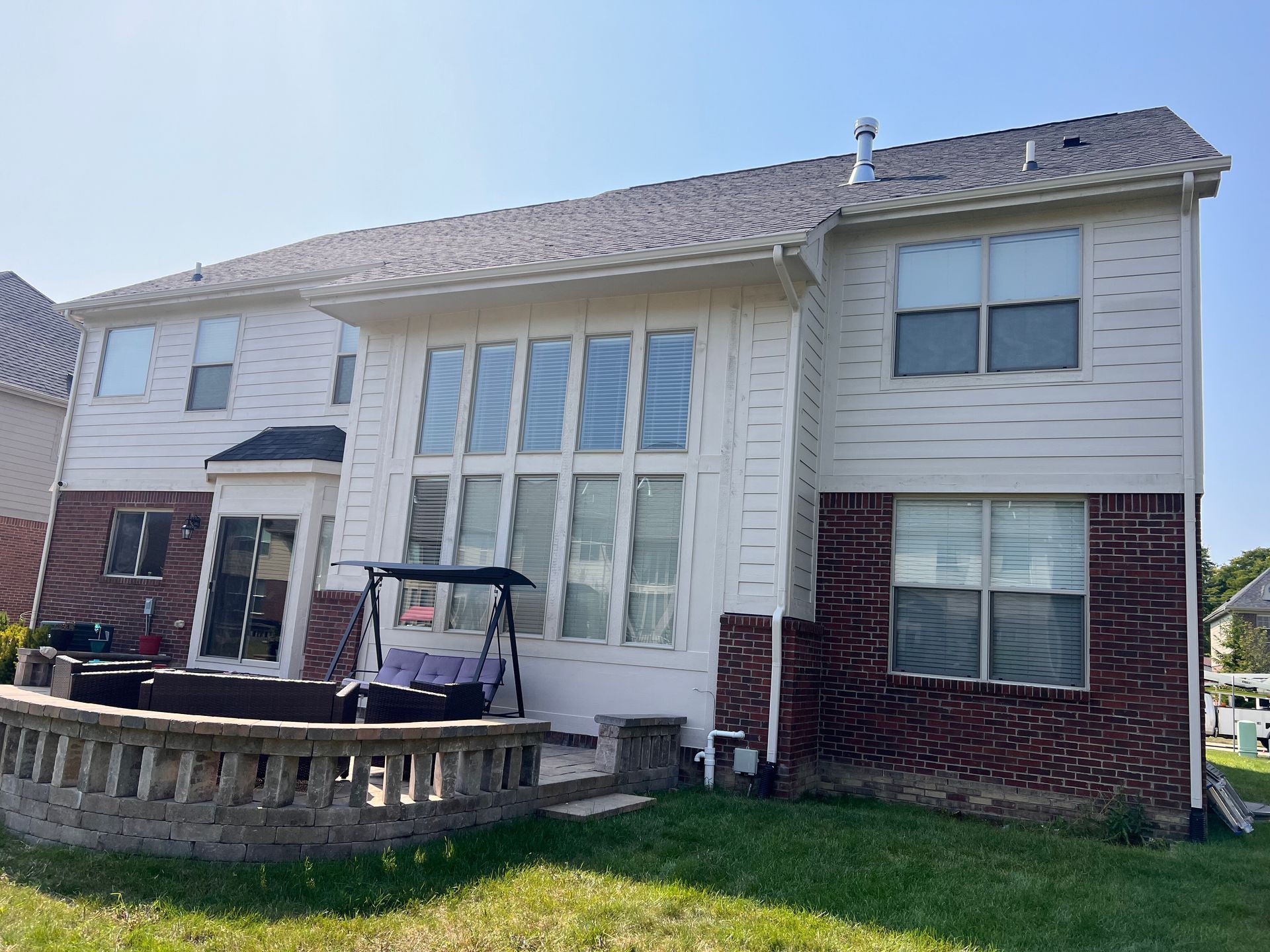 Back of a two-story house with white siding and brick, large windows, and a patio with a swing and railing.