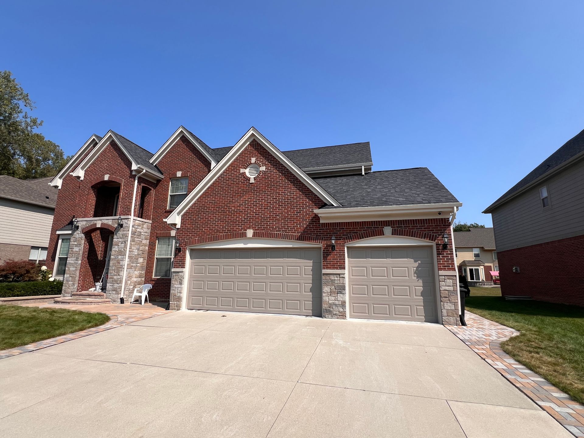 Red brick house with two-car garage, stone accents, and a paved driveway under a blue sky.