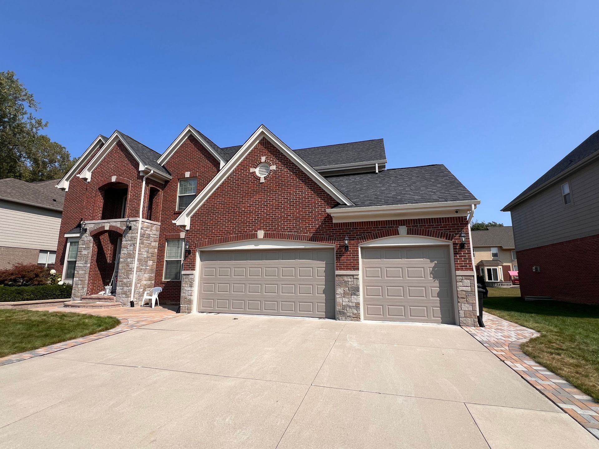 Brick house with two-car garage, gray doors, and a concrete driveway on a sunny day.