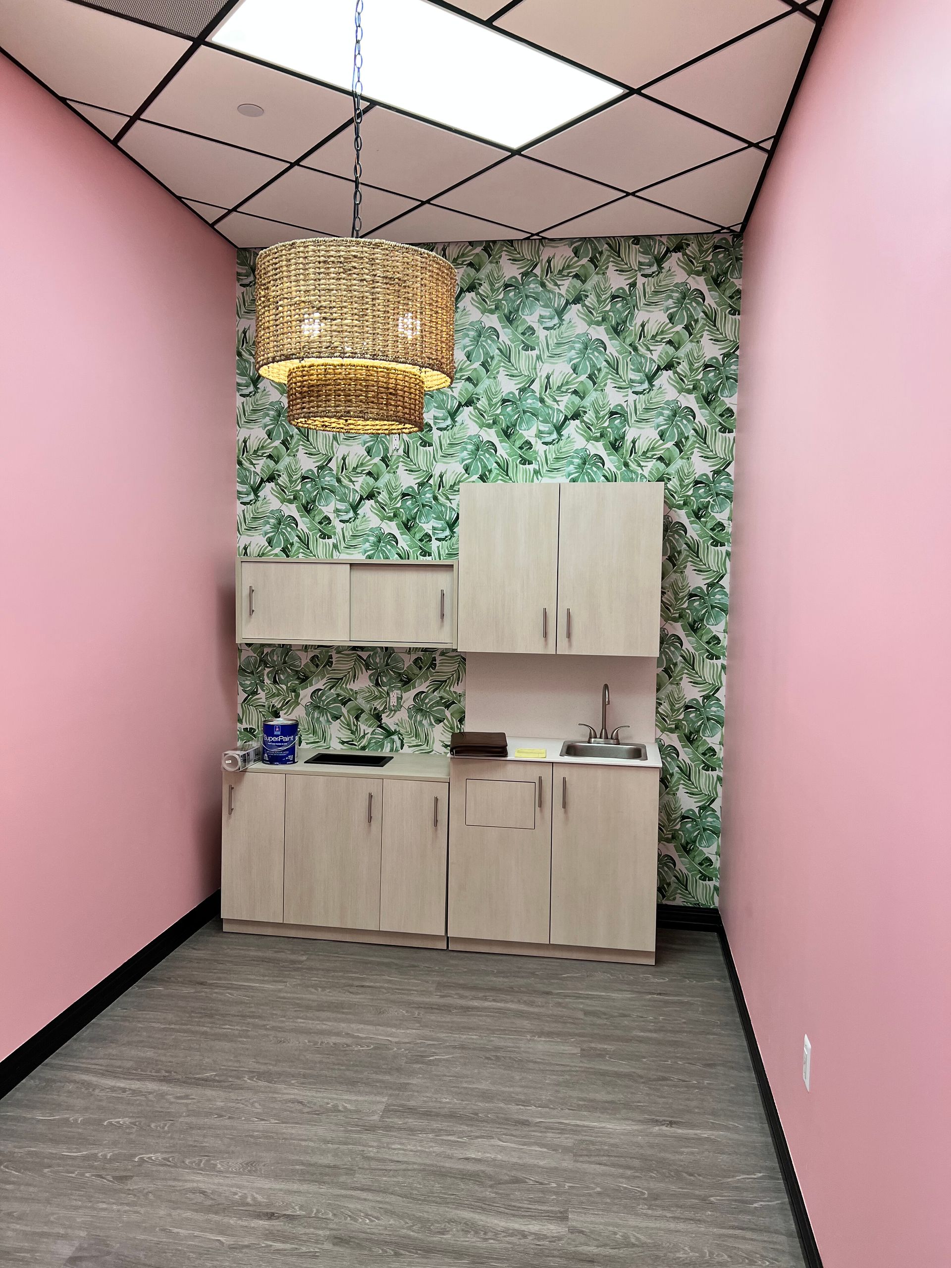 Pink-walled room with cabinets against a patterned wall, lit by a wicker pendant.