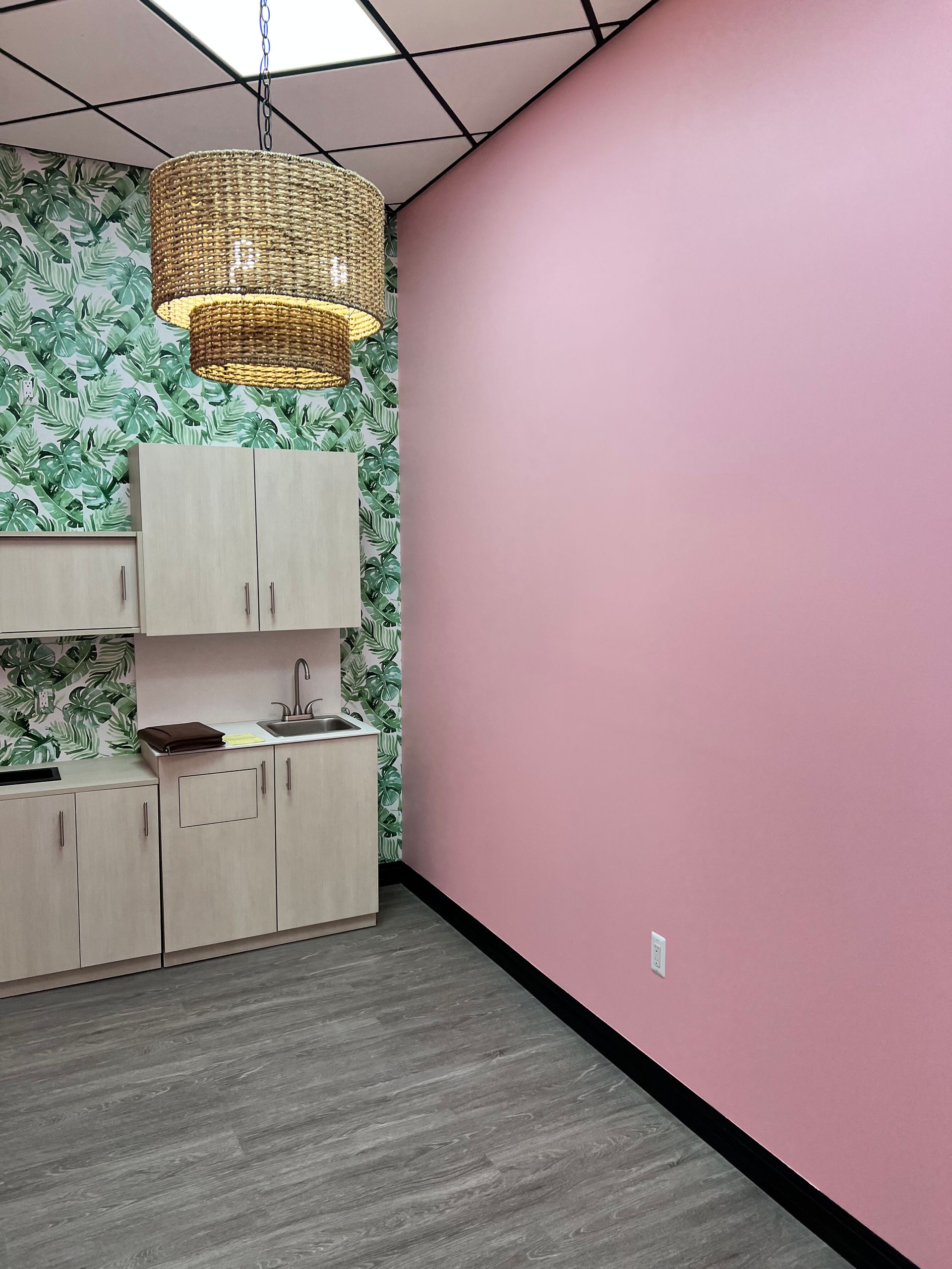 Room with light pink and patterned walls, cabinets, sink, and decorative light fixture.