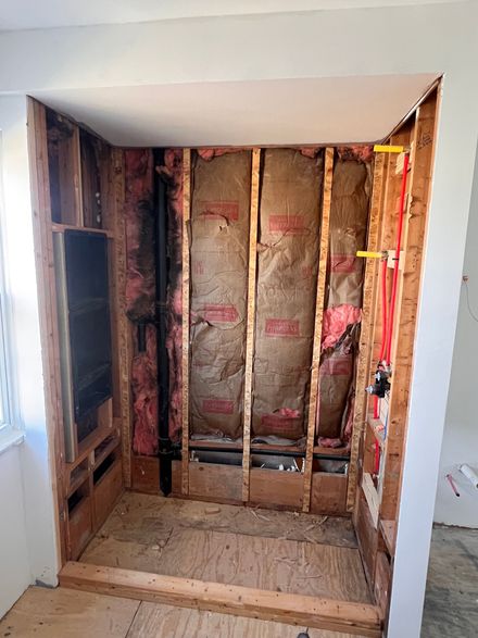 Bathroom shower frame under construction, insulation visible. Plumbing and water lines are present.