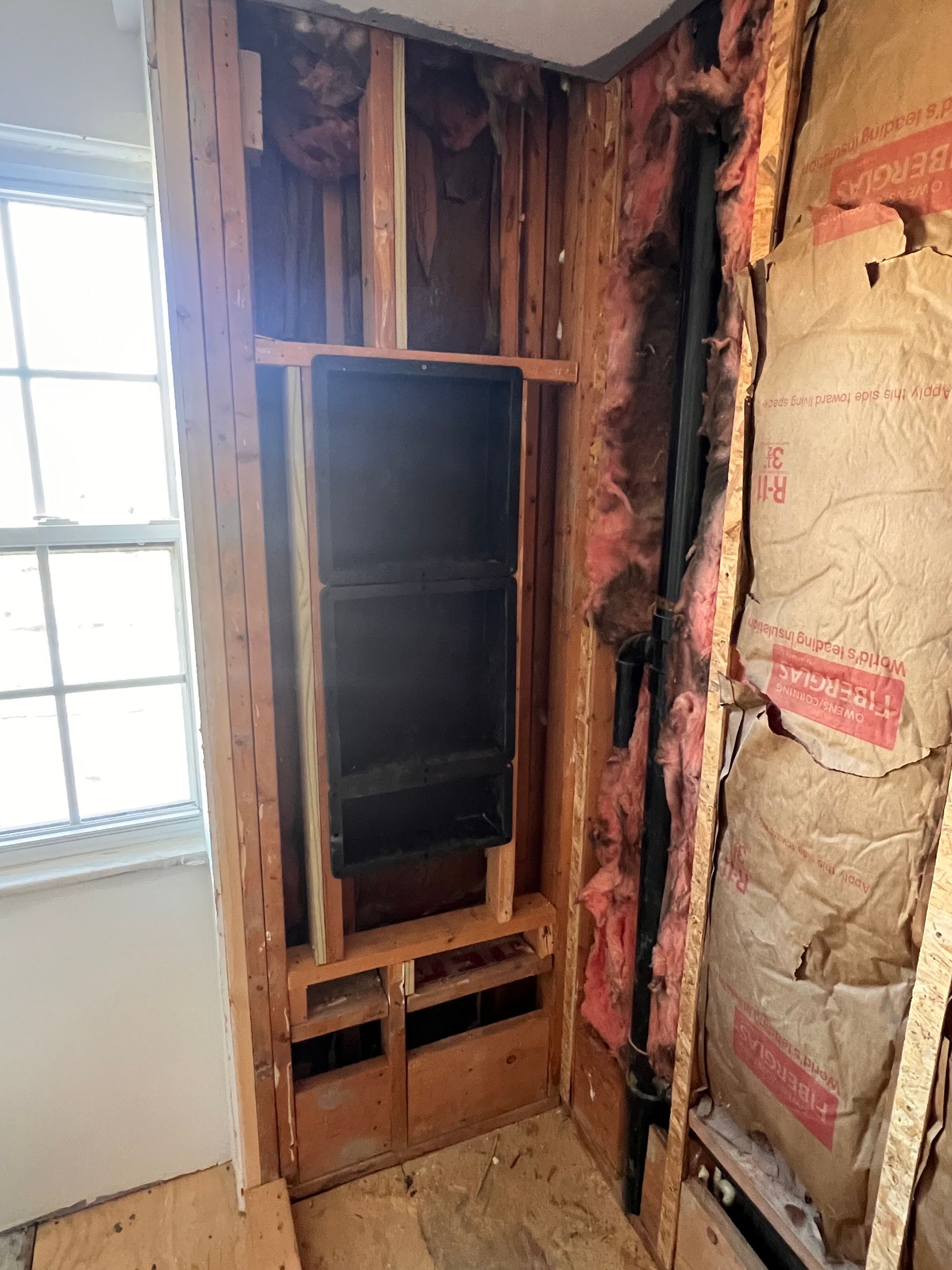 Interior wall studs exposed, showing a recessed cabinet area and plumbing. Insulation and window visible.
