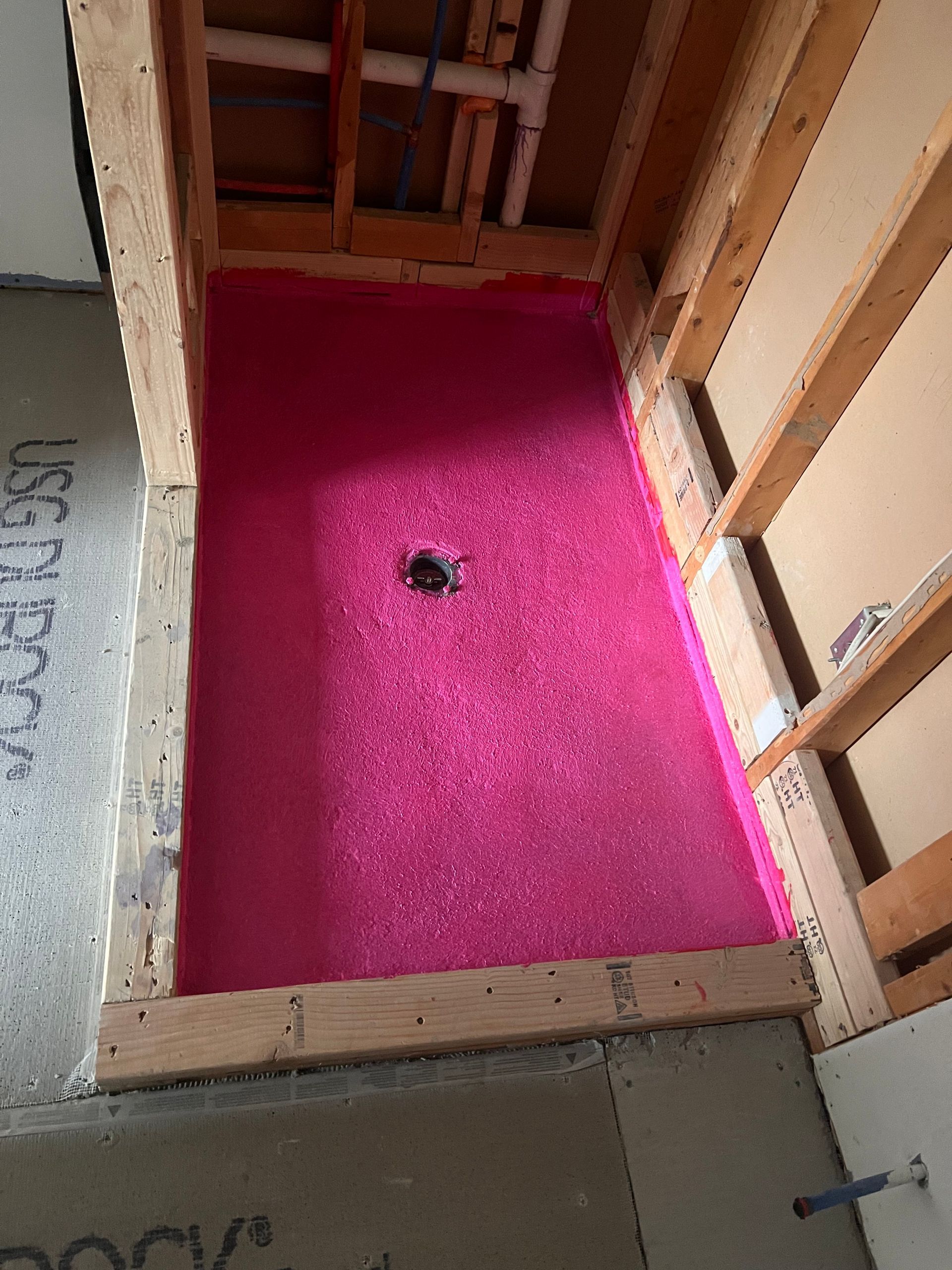 Pink shower pan, set in wooden frame, with drain, prepared for tiling.