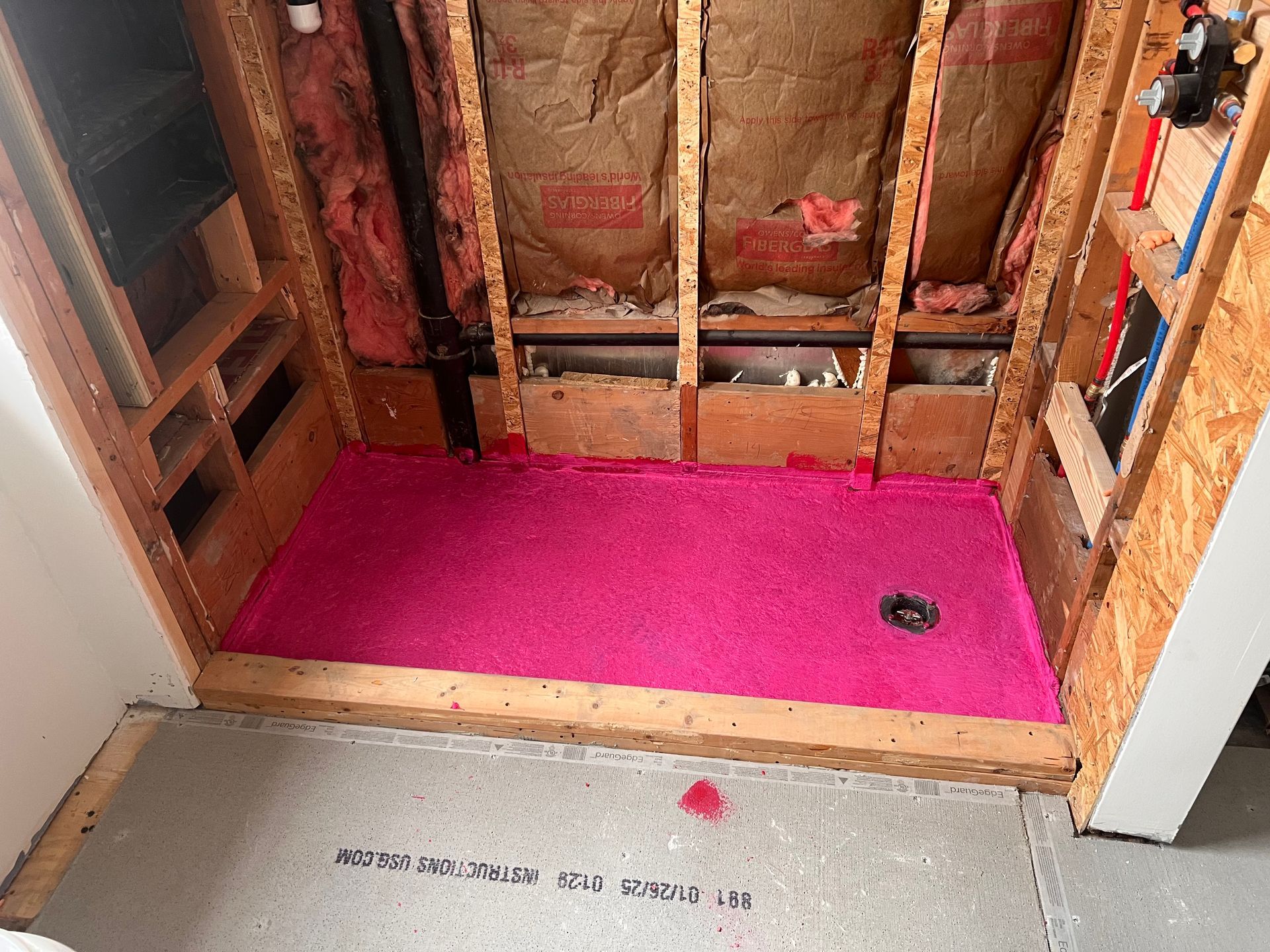 Pink shower pan installed in a framed bathroom with exposed insulation.