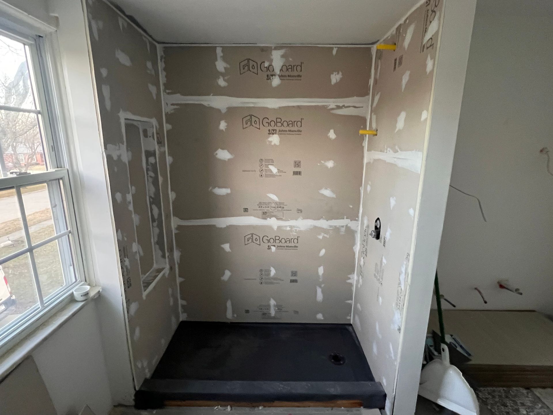 Shower stall under construction, gray cement board walls, black shower base, unfinished.