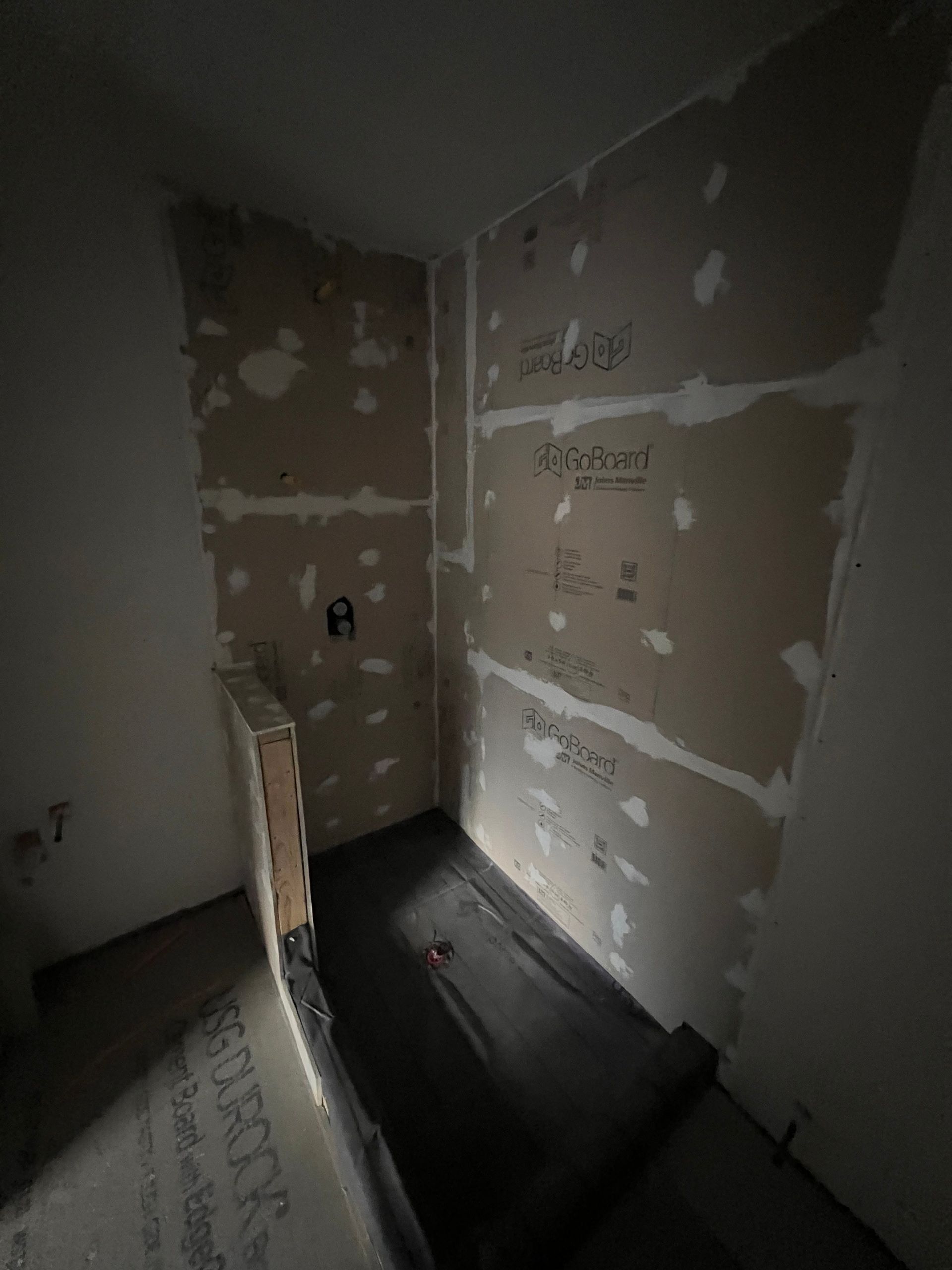 Unfinished shower stall with backer board installed on walls. Black shower pan.