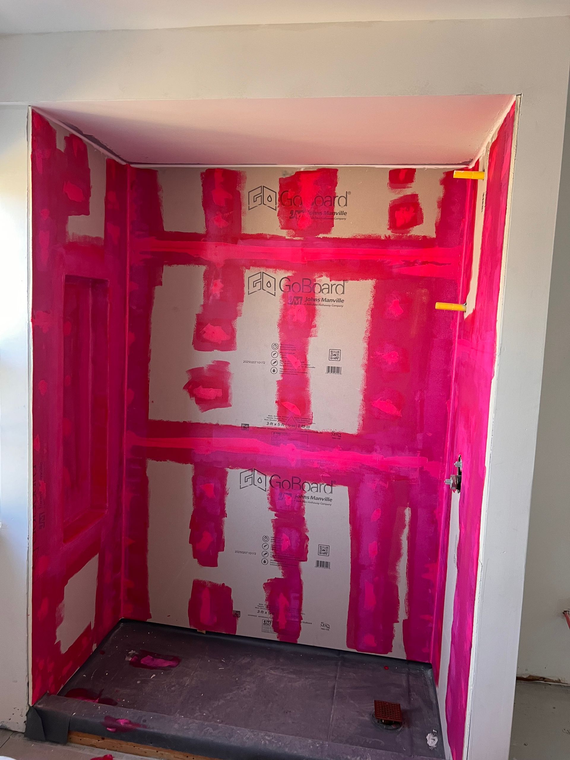 Pink waterproof membrane applied to the interior of a shower niche, ready for tile installation.