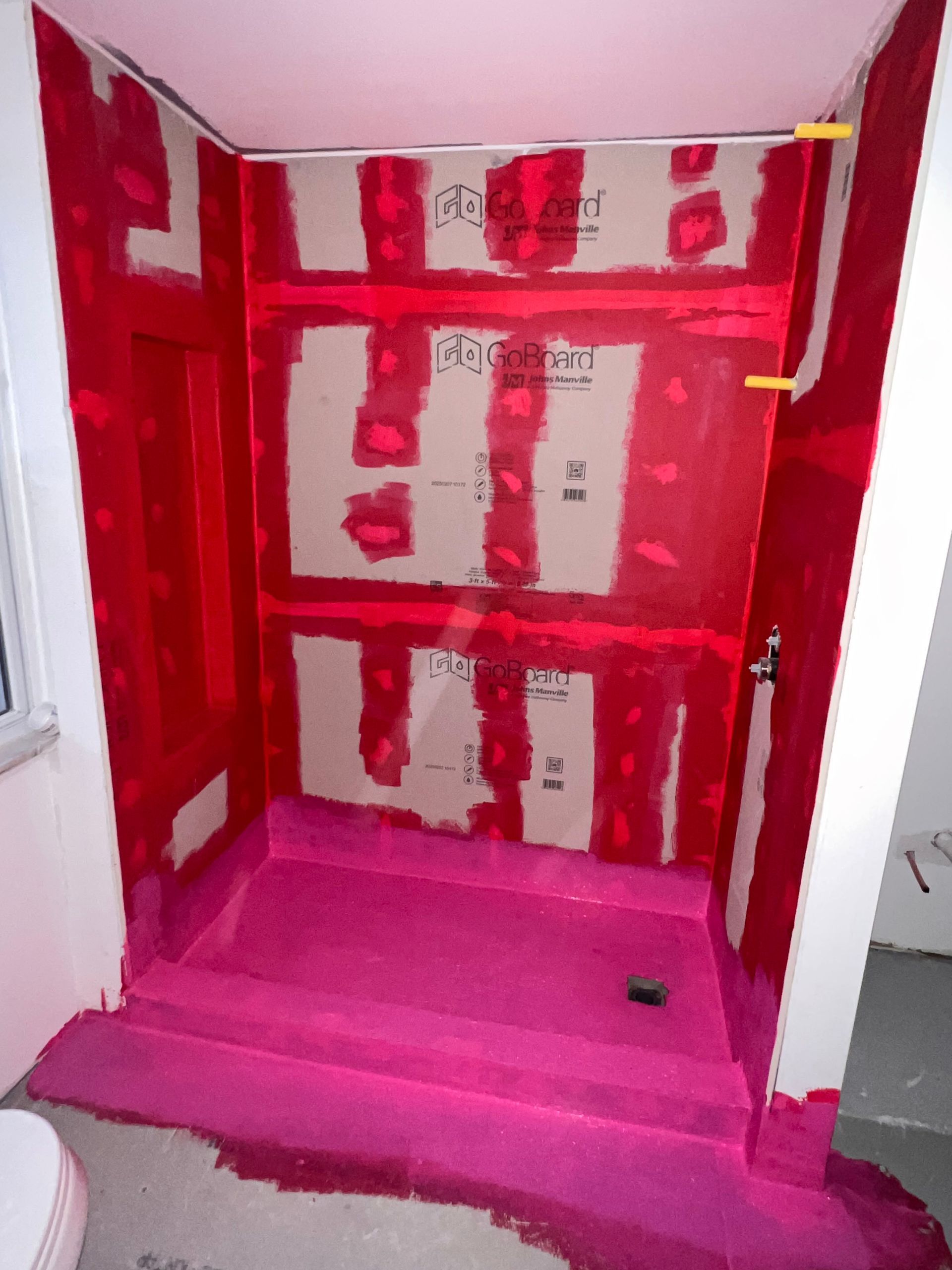 Shower stall under construction, pink waterproofing membrane and panels, in a bathroom.