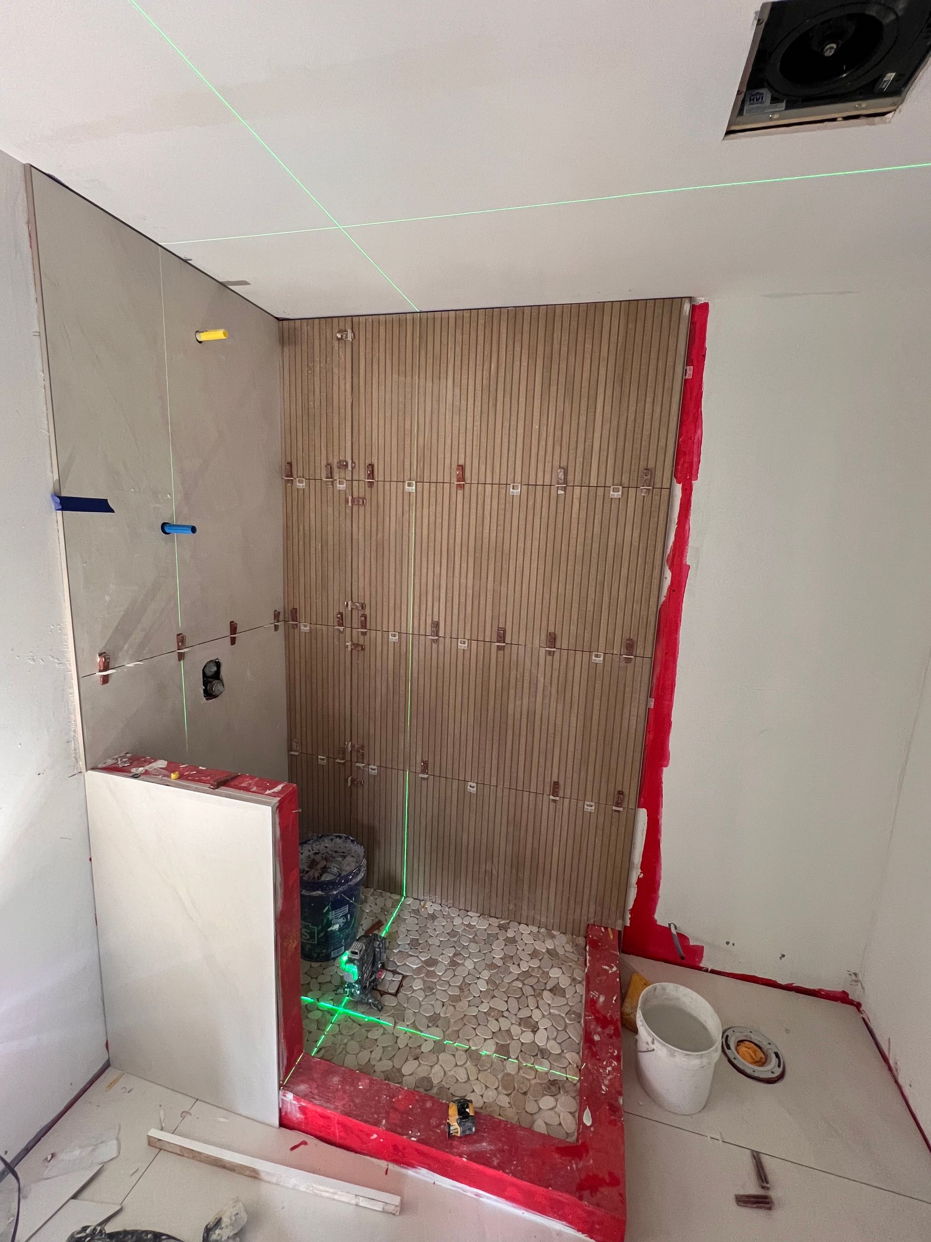 Bathroom under construction with green laser level. Walls are partially tiled; red waterproofing visible.