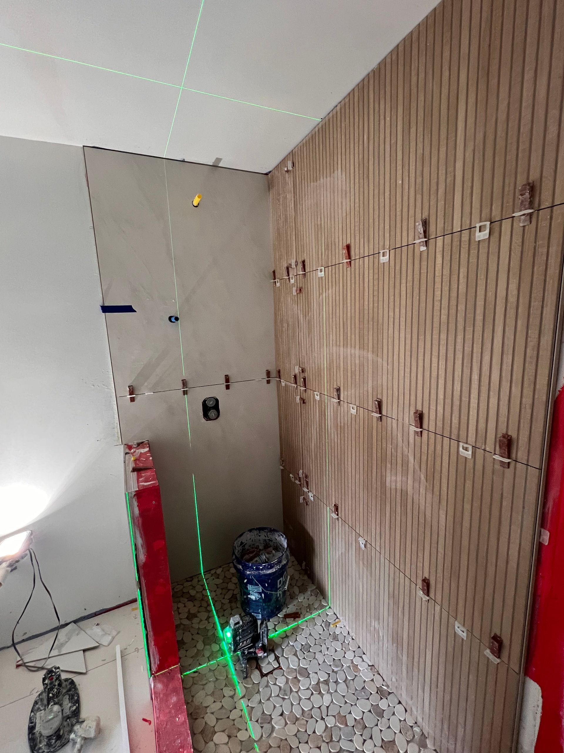 Bathroom renovation in progress; tiles being installed on walls; green laser level and spacers visible.
