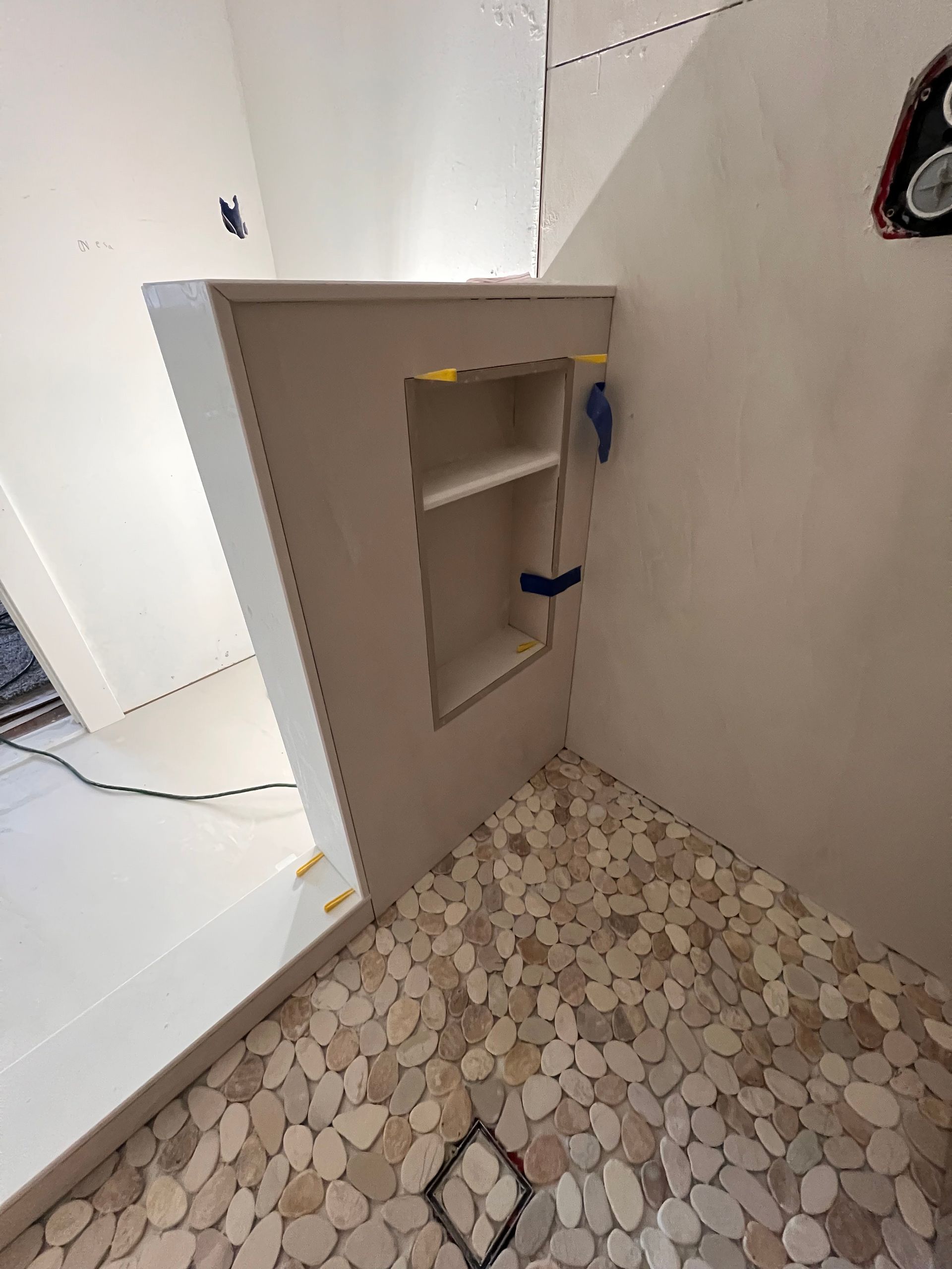 Shower corner under construction with stone floor, recessed shelf, and unfinished walls.