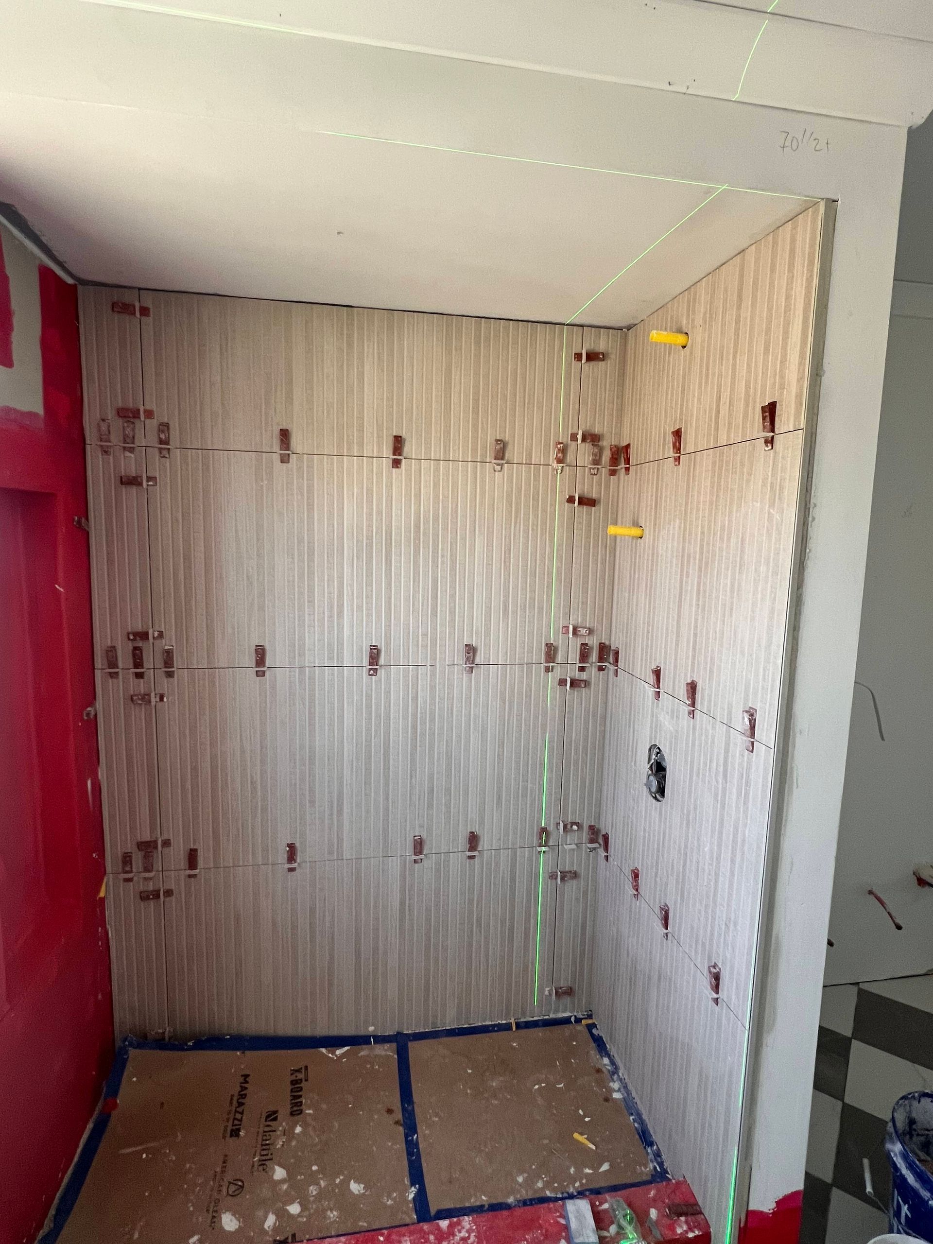 Interior of a shower stall under construction; walls are covered in light wood-look panels, pink waterproof walls, and blue tape on the floor.