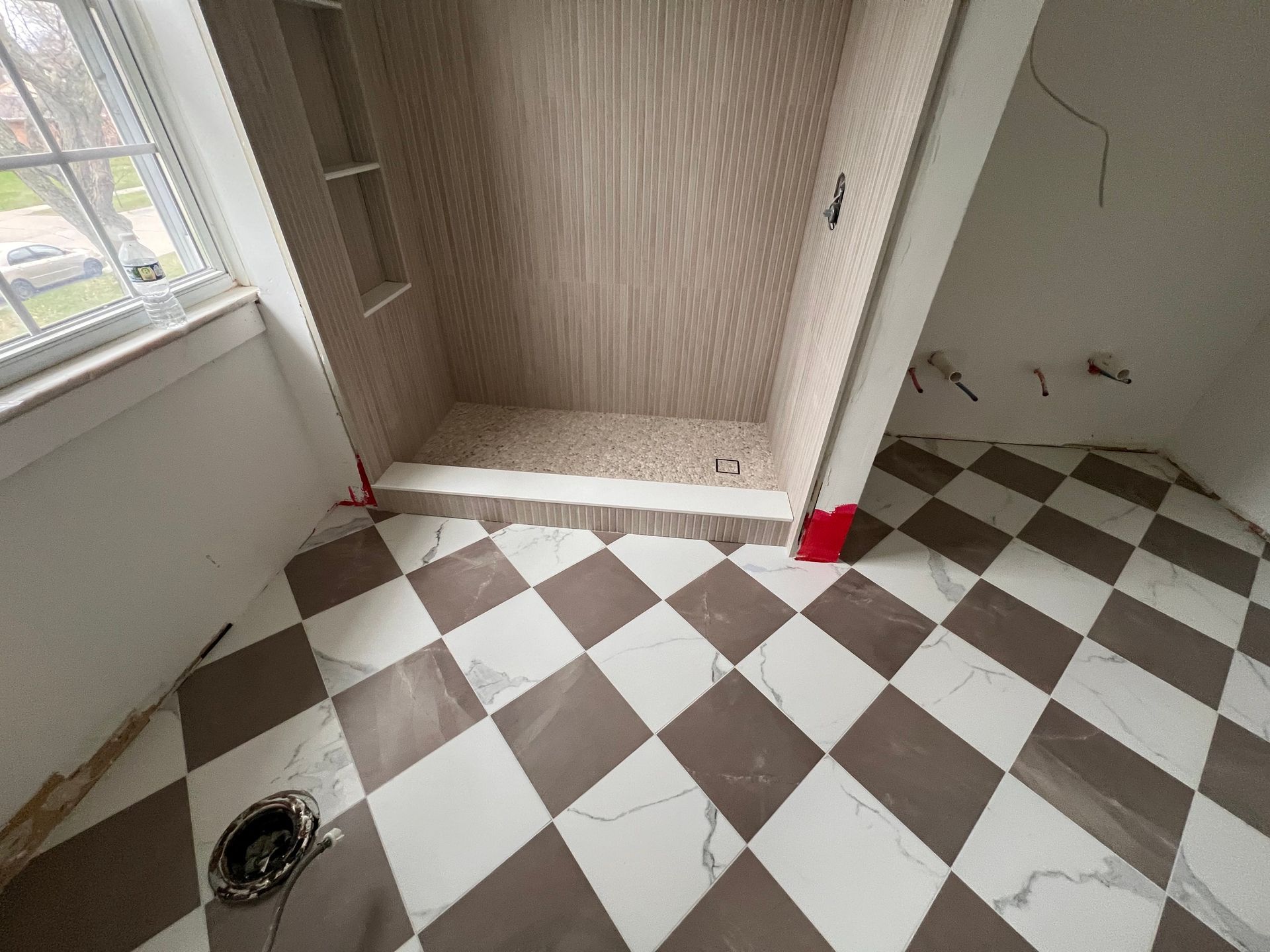 Bathroom with diamond-patterned tile floor, shower stall with light wood-look tile, and open doorway.