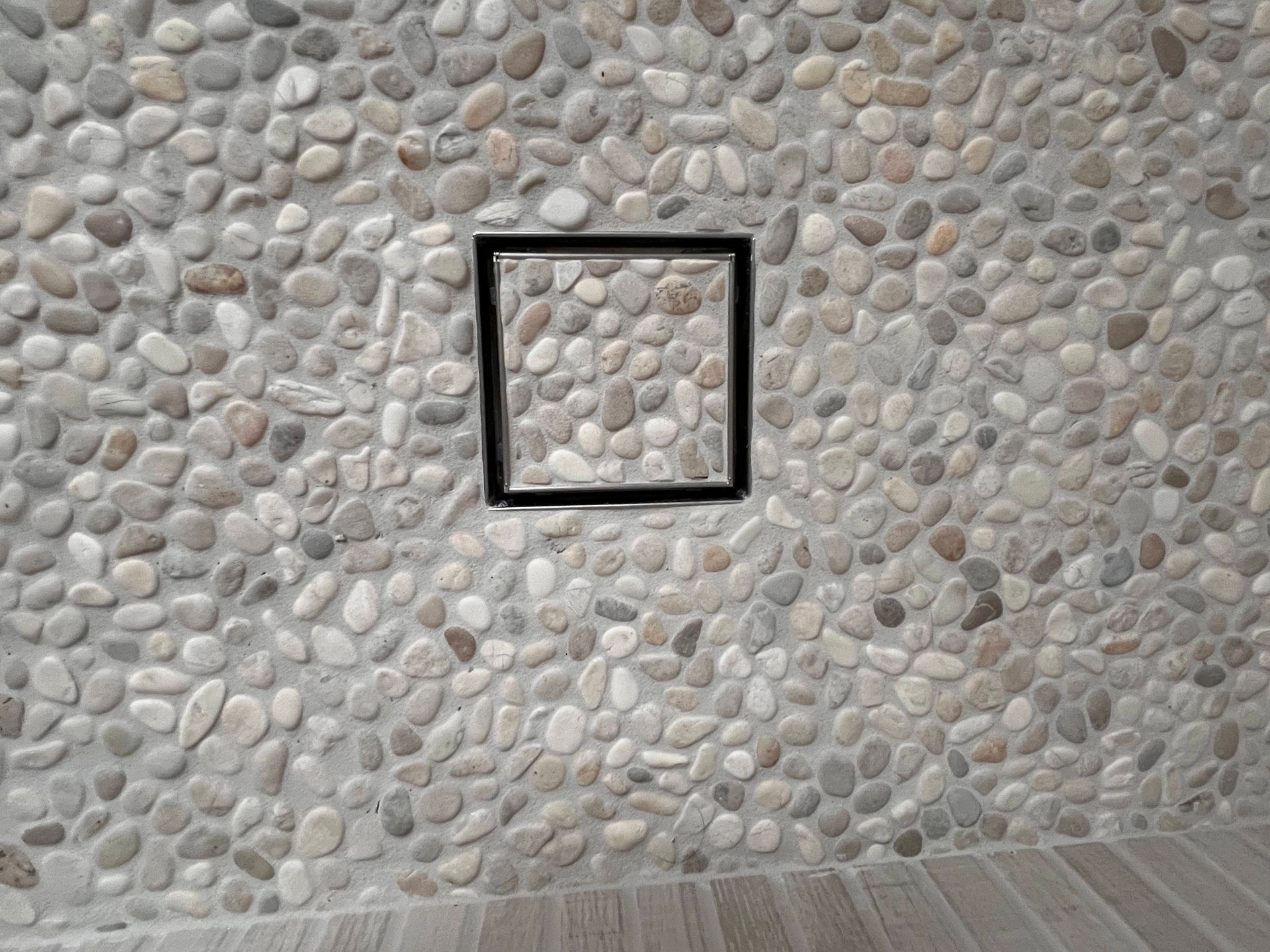 Pebble-covered shower floor with a square drain. Brown and gray stones are set in concrete.