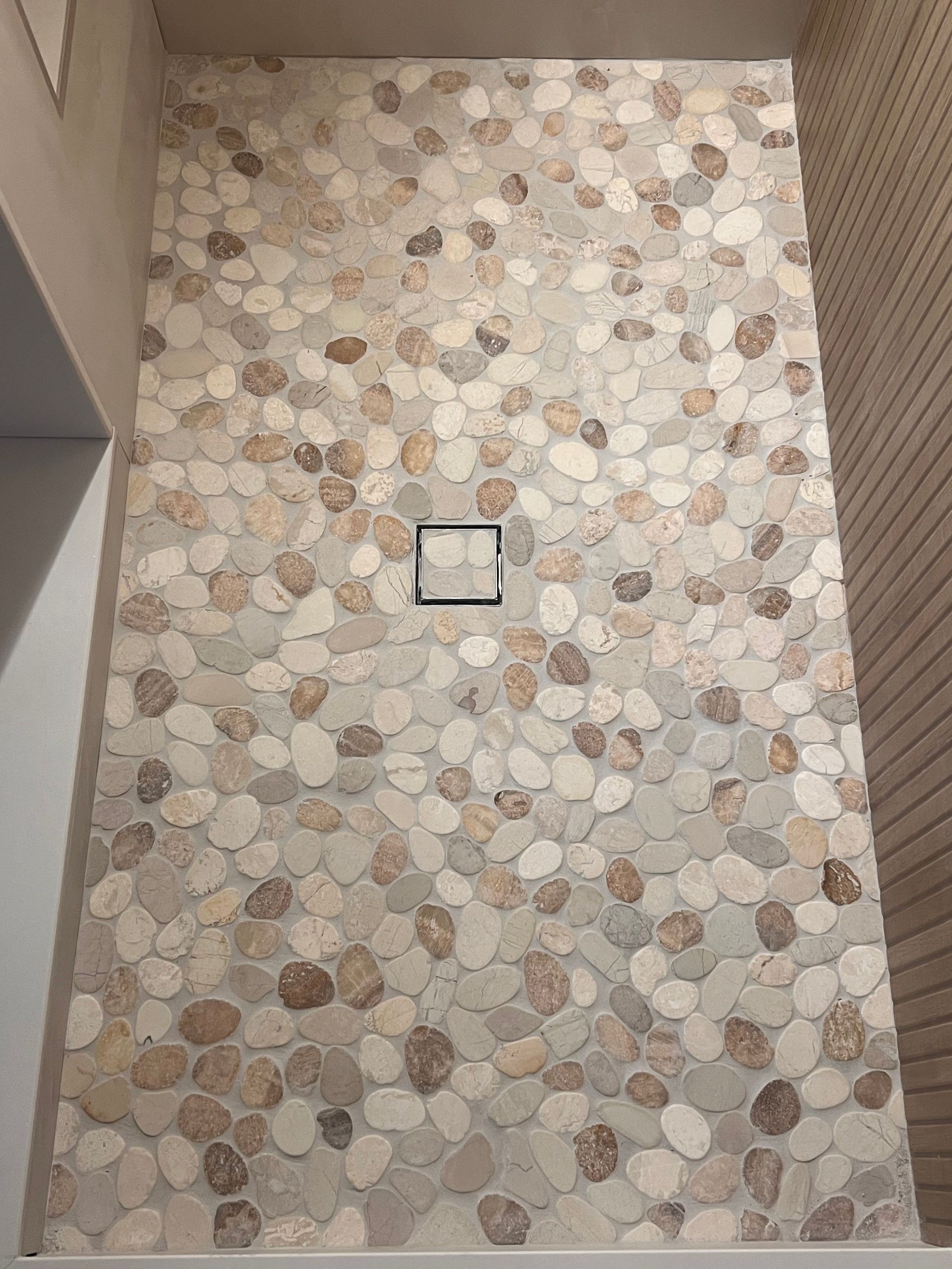 Shower floor with beige and brown river rock tiles and a square drain.