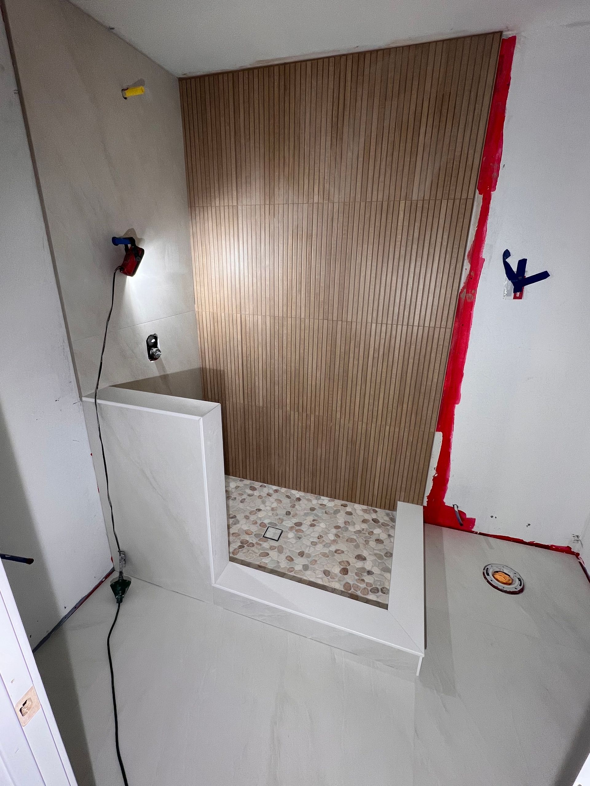 Bathroom shower under construction with light wood paneling, gray tile, and open entryway.