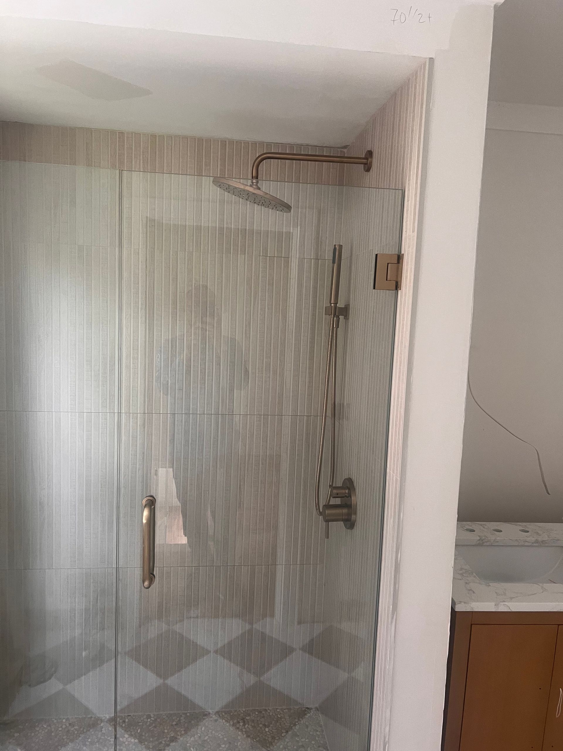 Shower enclosure with glass door and rain shower head. Tiles are beige and the floor is checkered.