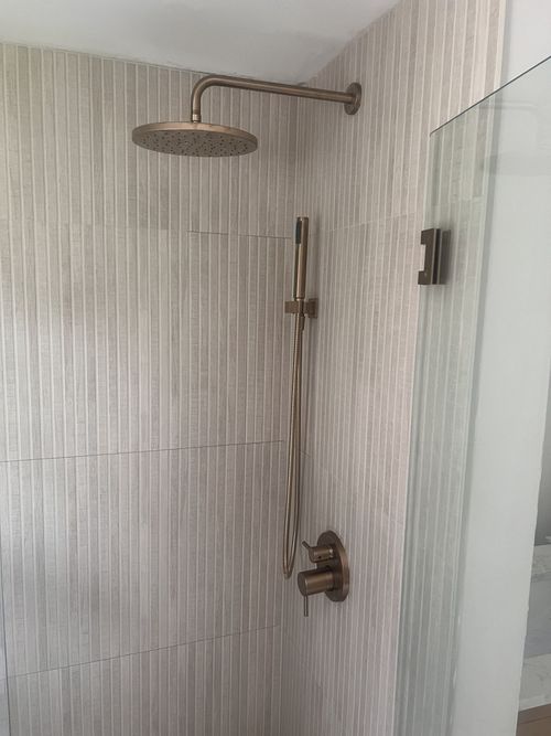 Shower with bronze fixtures against textured, light-colored wall. Glass shower door to the right.