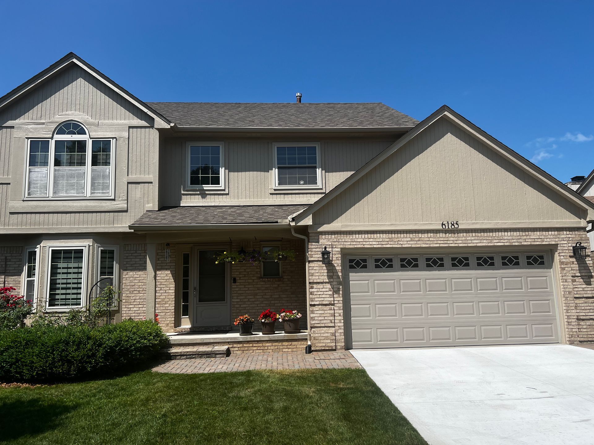 Beige house with light gray garage door, stone accents, green lawn, and blue sky.