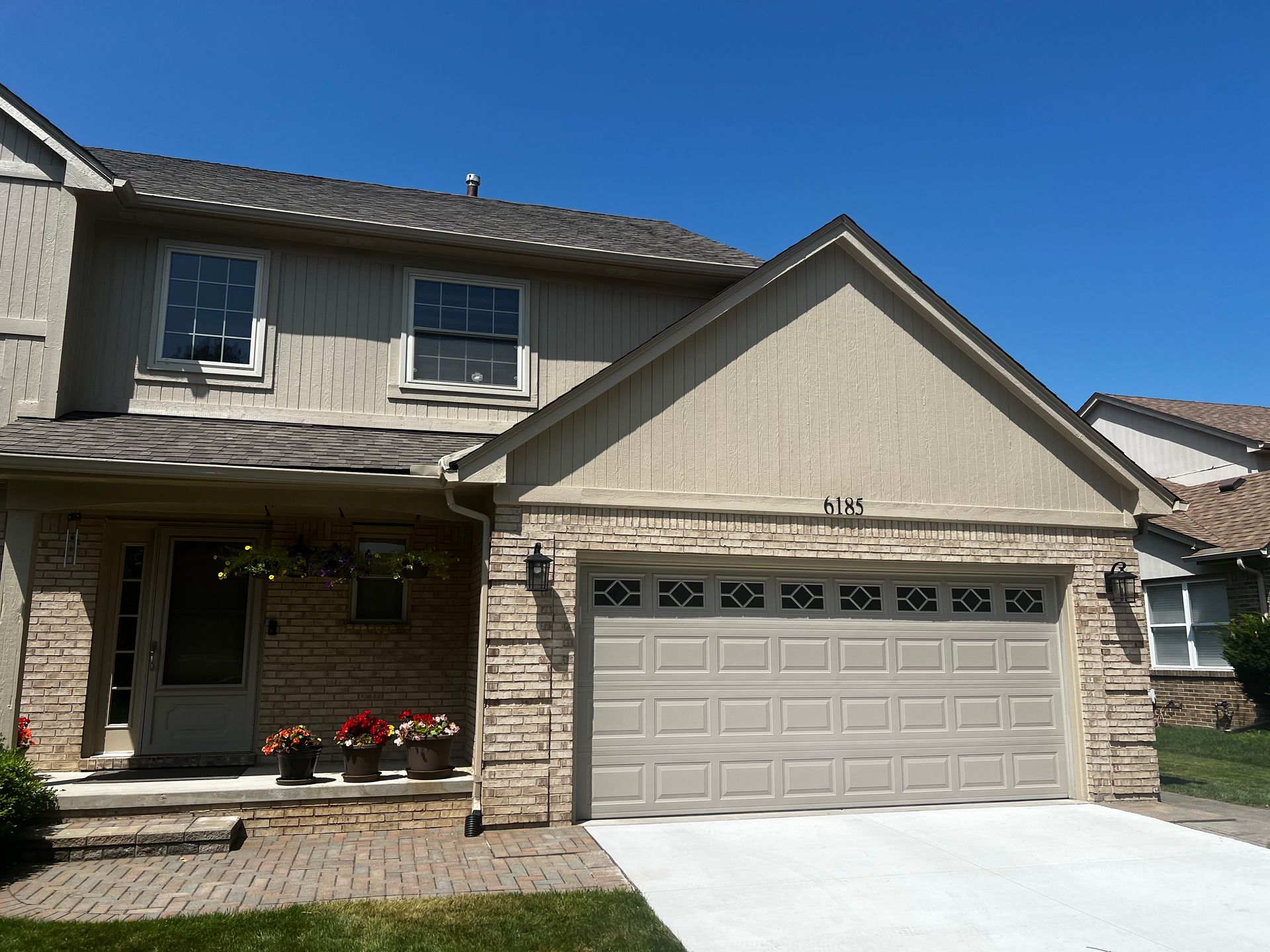 Two-story beige house with a stone facade garage, and a blue sky overhead.