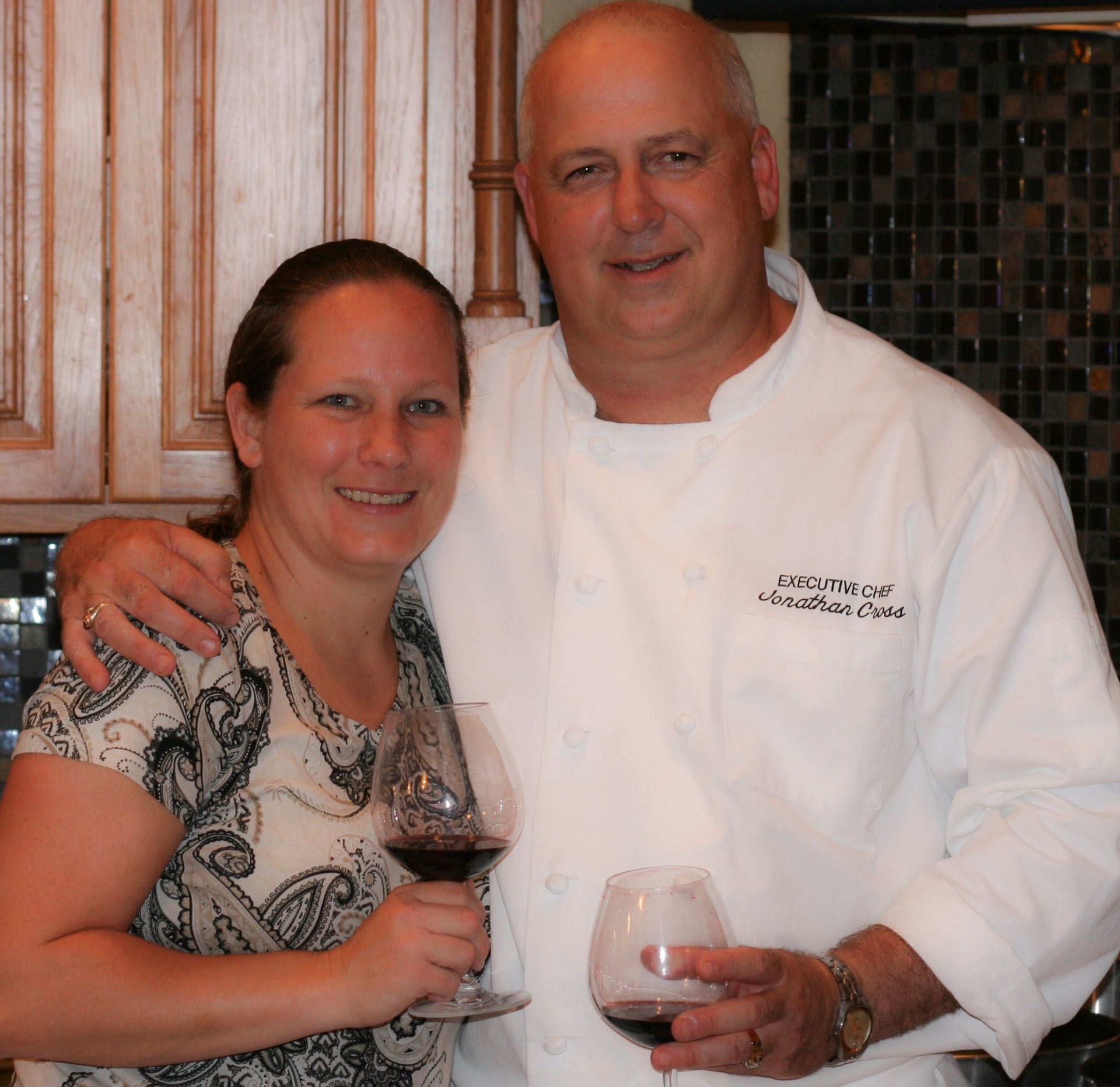 A man in a chef 's uniform stands next to a woman holding a glass of wine