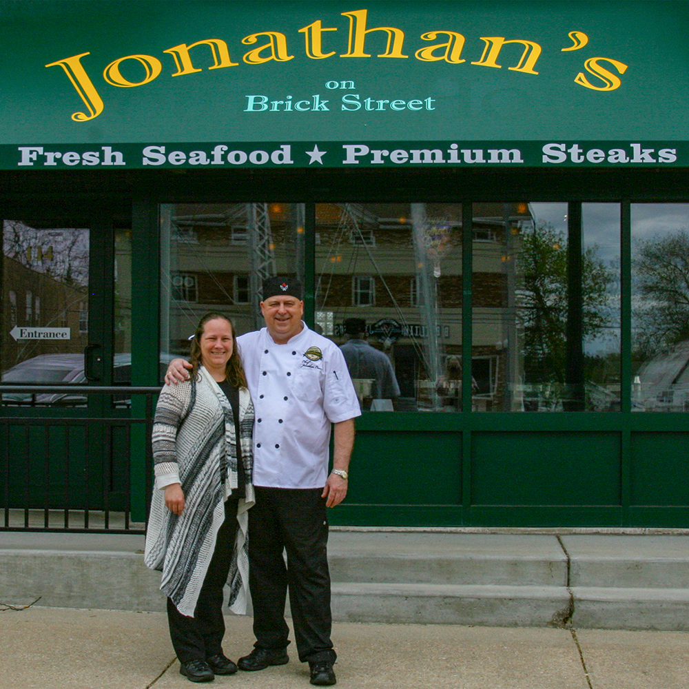A man and woman standing in front of a restaurant called jonathan 's on brick street