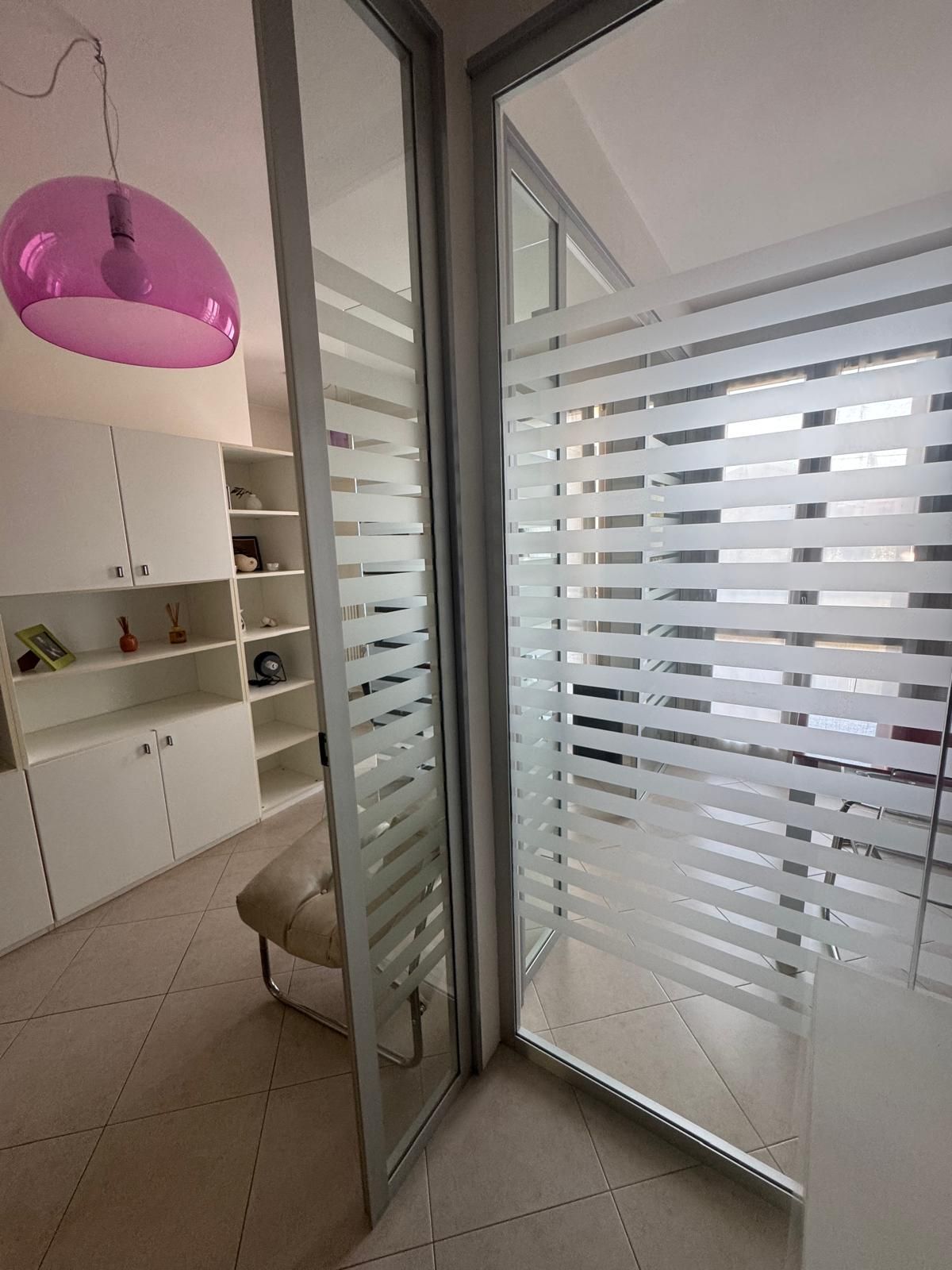 Luminoso corridoio con porta scorrevole in vetro satinato, scaffali bianchi a incasso e lampada a sospensione rosa.