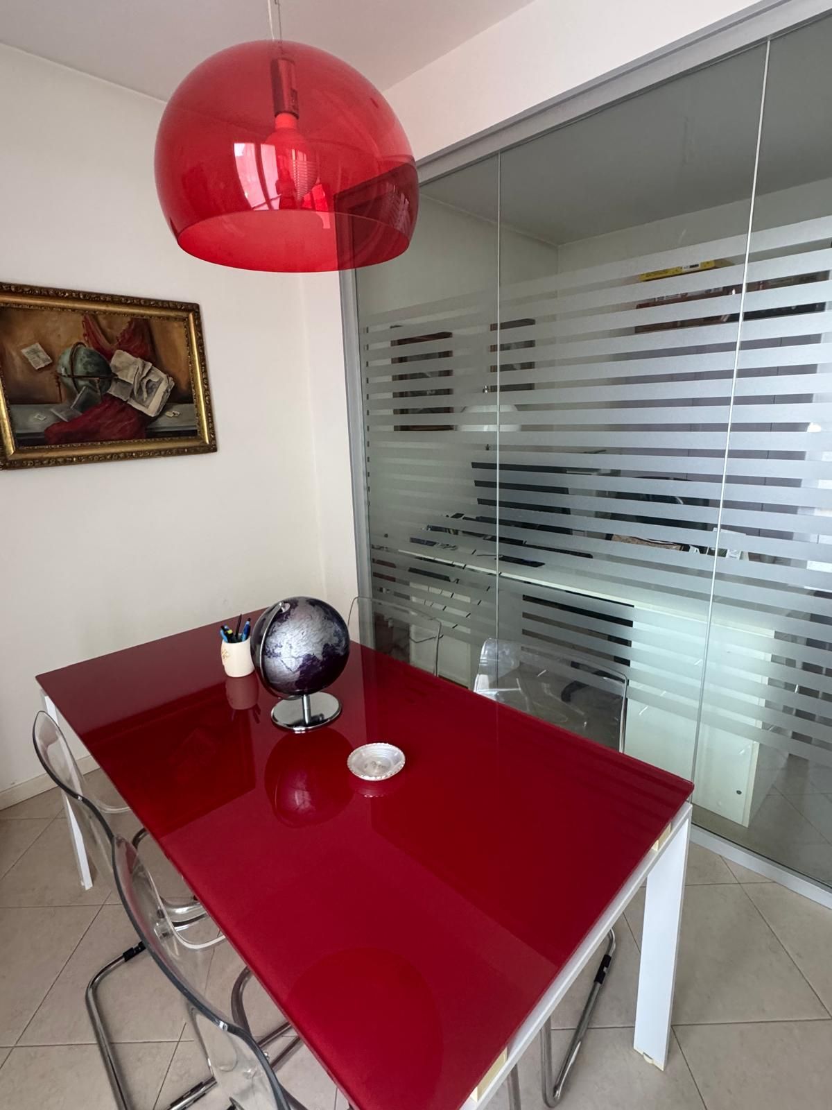 Tavolo da pranzo rosso con sedie cromate, lampada a sospensione, decorazioni murali e parete divisoria in vetro in una stanza moderna