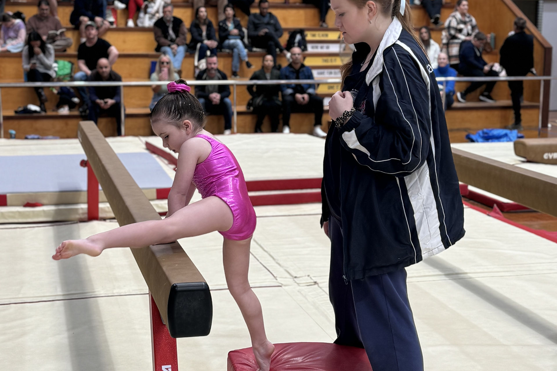 A young girl is sitting on a balance beam in a gym.