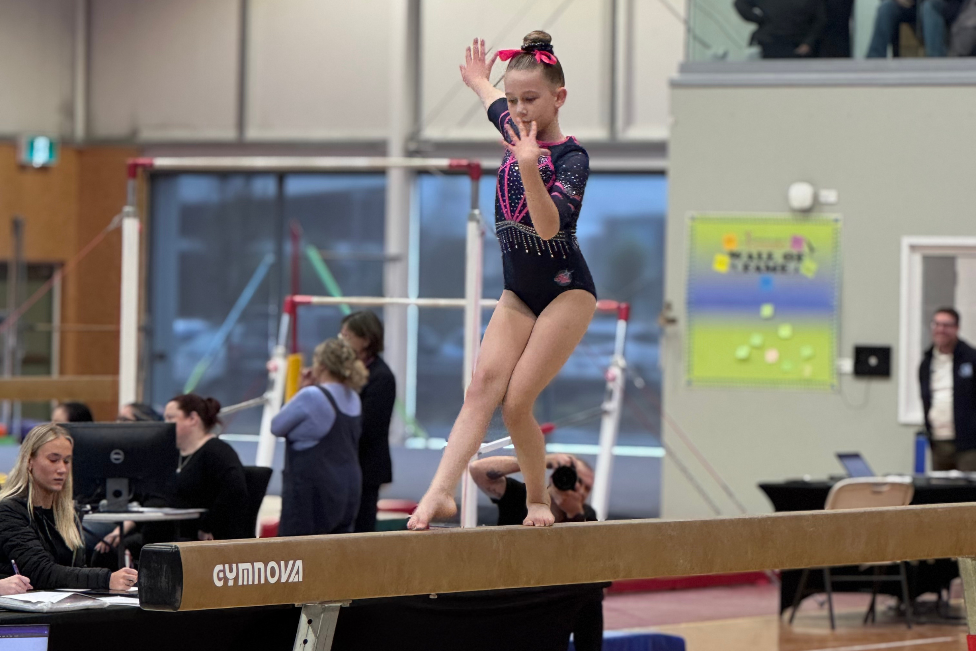 A female gymnast is standing on a balance beam.