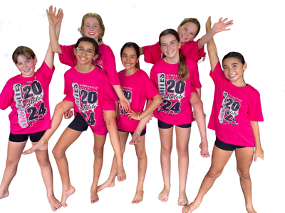 Group of girls in pink shirts and black shorts, posing with smiles and raised arms.