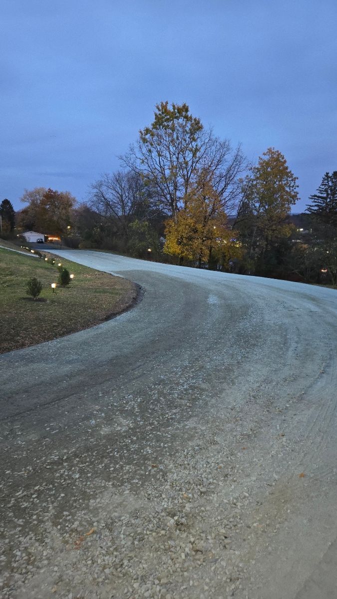 Gravel road curves uphill toward trees with muted fall foliage under a dusk sky.