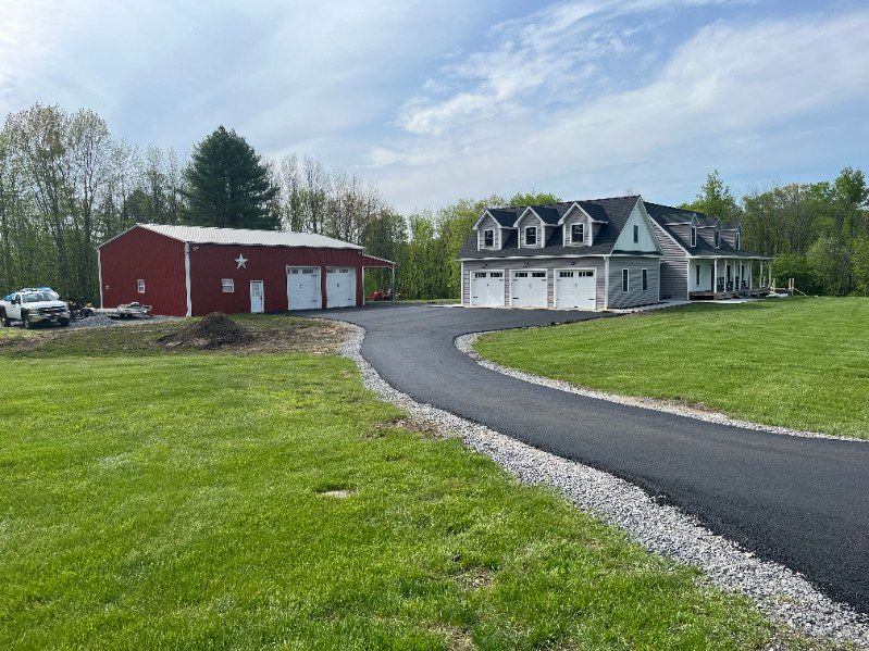 House and red garage with asphalt driveway on green lawn under cloudy sky.