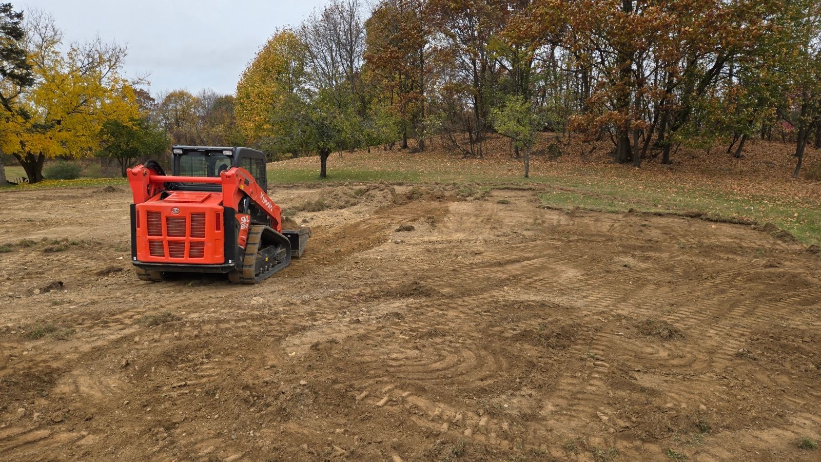 Orange skid steer on dirt clearing, trees in background.