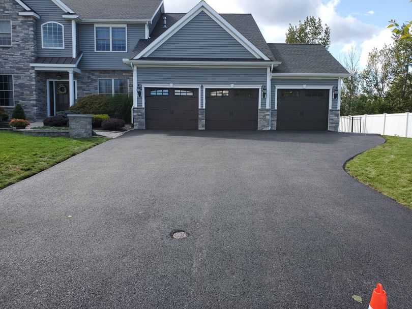 Asphalt driveway leading to a three-car garage of a two-story gray house.