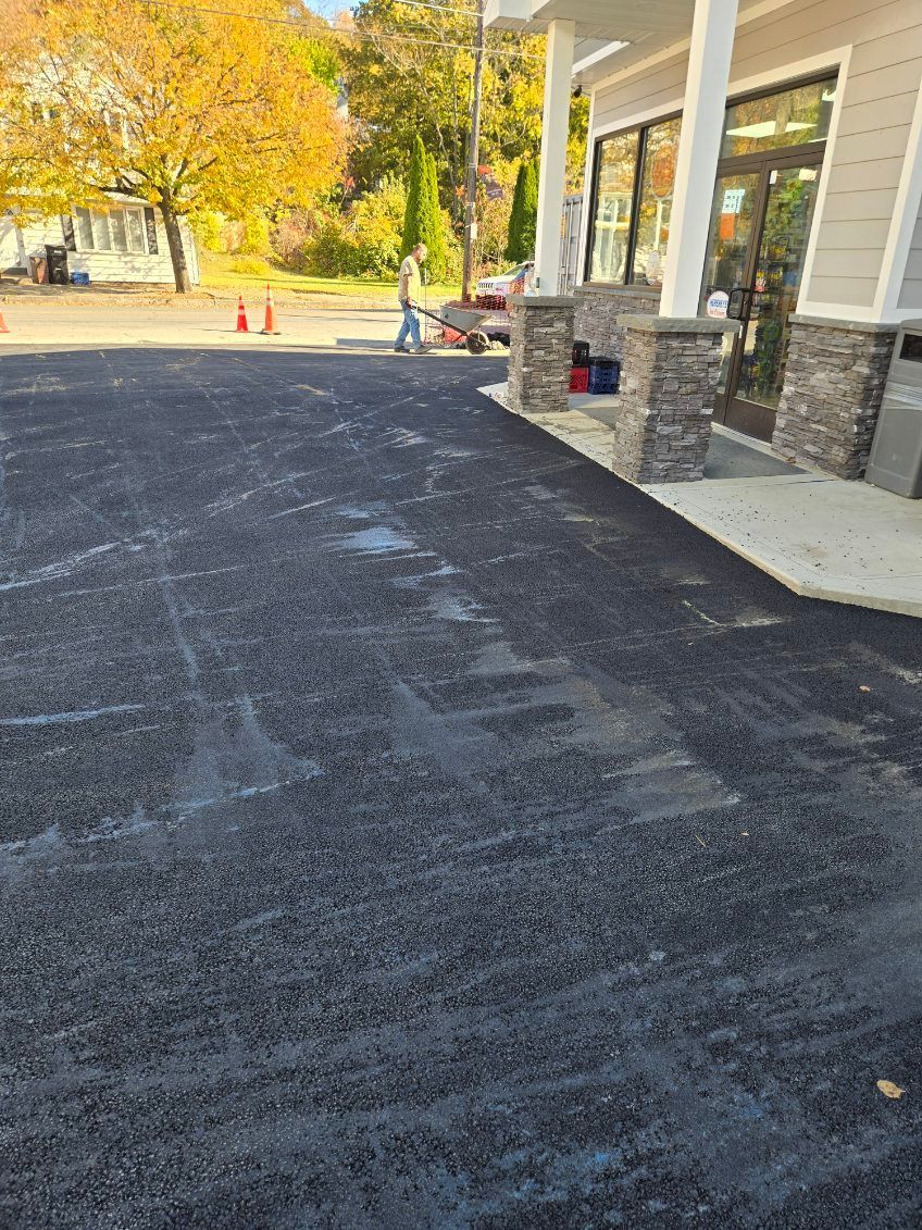 Asphalt parking lot next to a building with stone columns. A person walks in the distance.