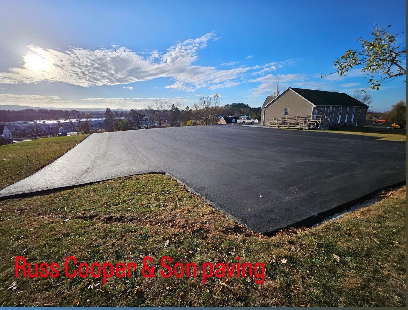 Newly paved asphalt area with a building, and a blue sky with clouds.