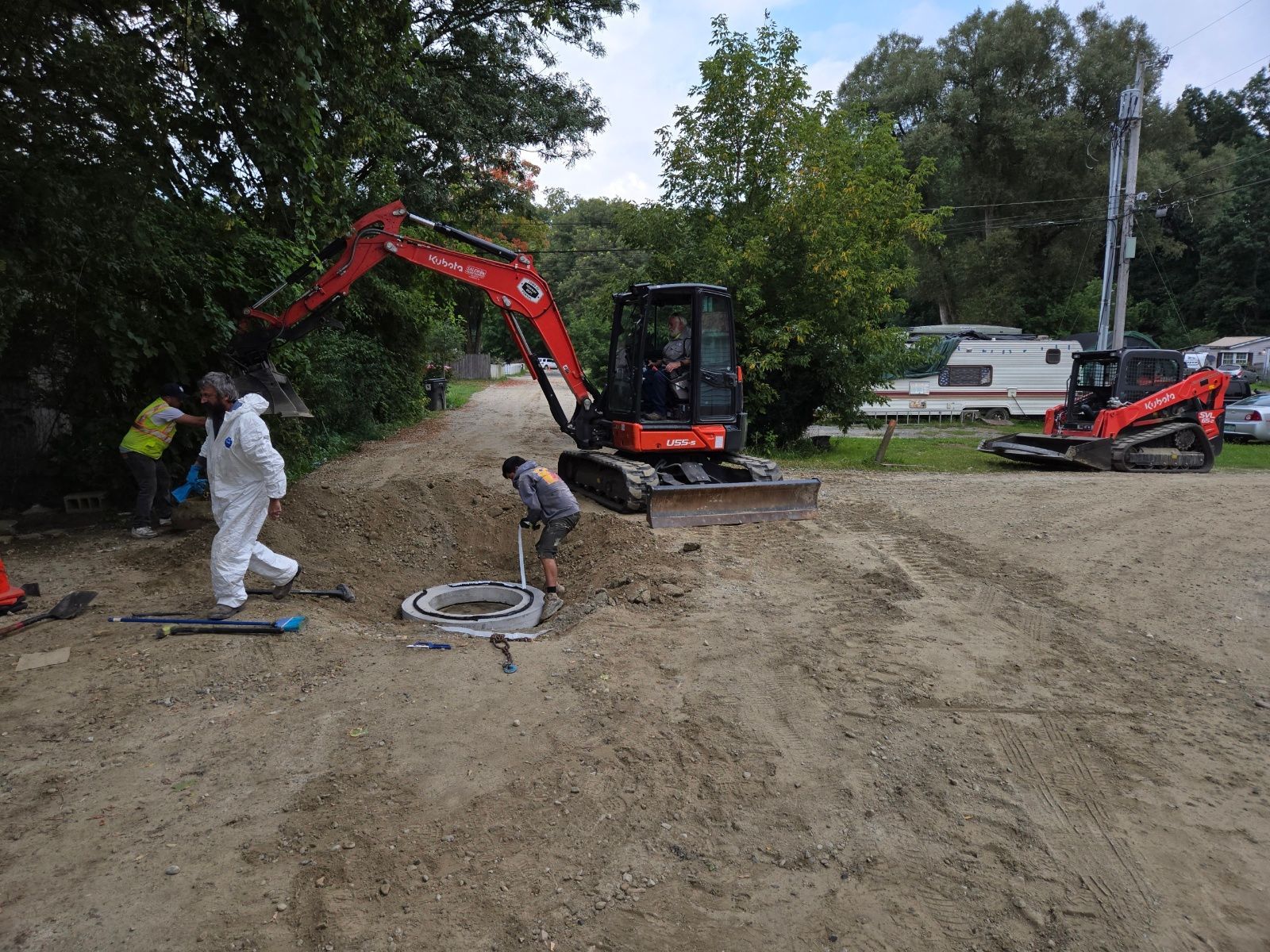 Construction workers around an excavator digging near a concrete structure outdoors.