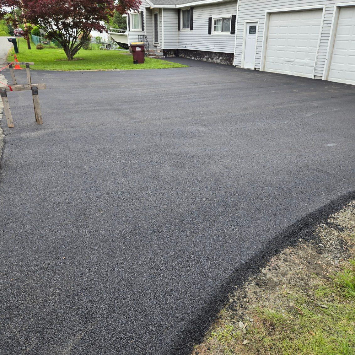 Newly paved asphalt driveway in front of a light gray house with a two-car garage.
