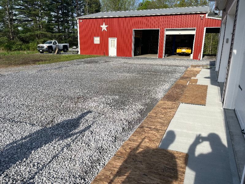 Red barn with gravel driveway. A yellow car is in one garage bay.