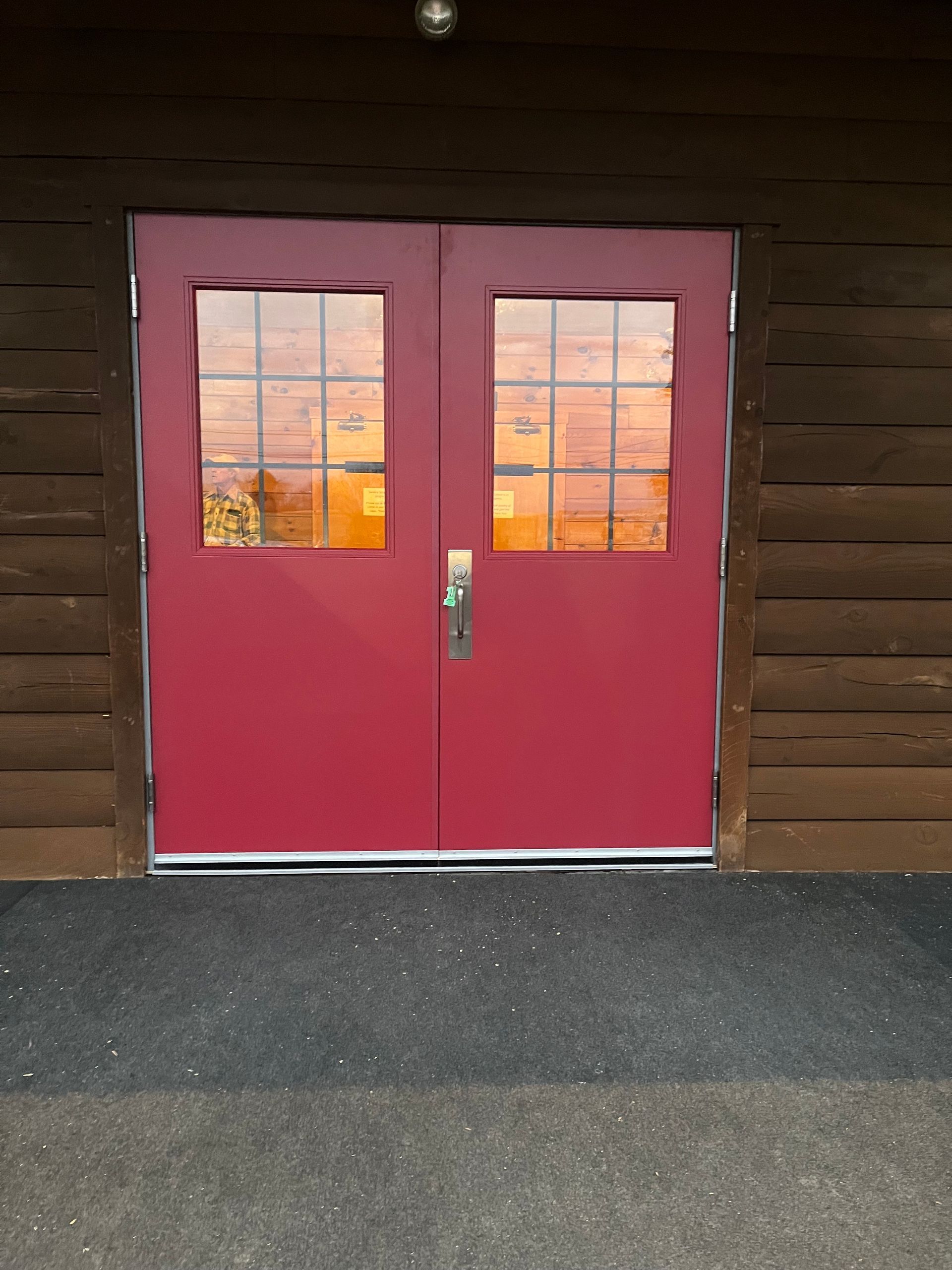 A set of red double doors with multi-pane windows set into a brown log building exterior.